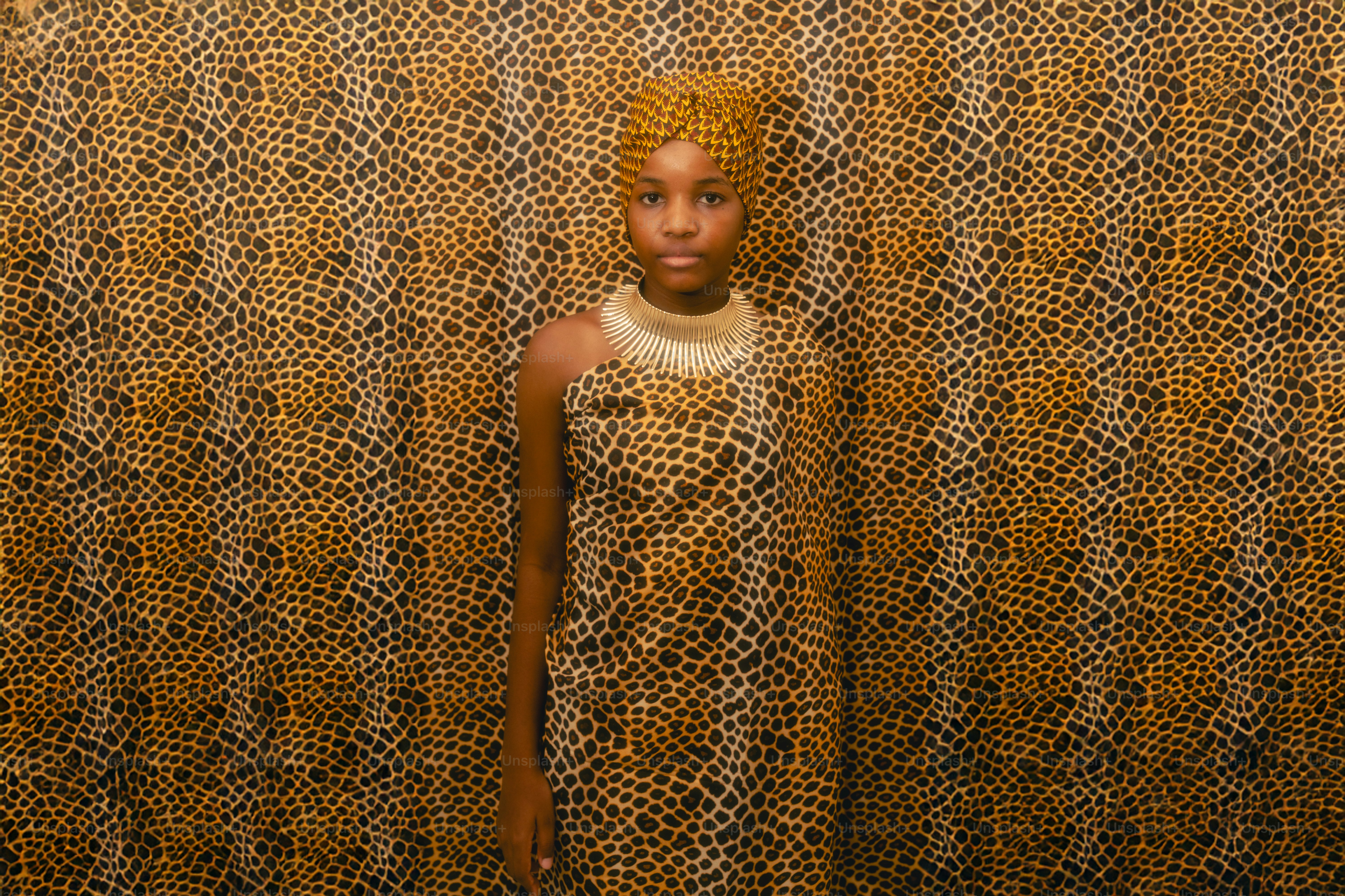Young girl in traditional african attire stands against patterned background.