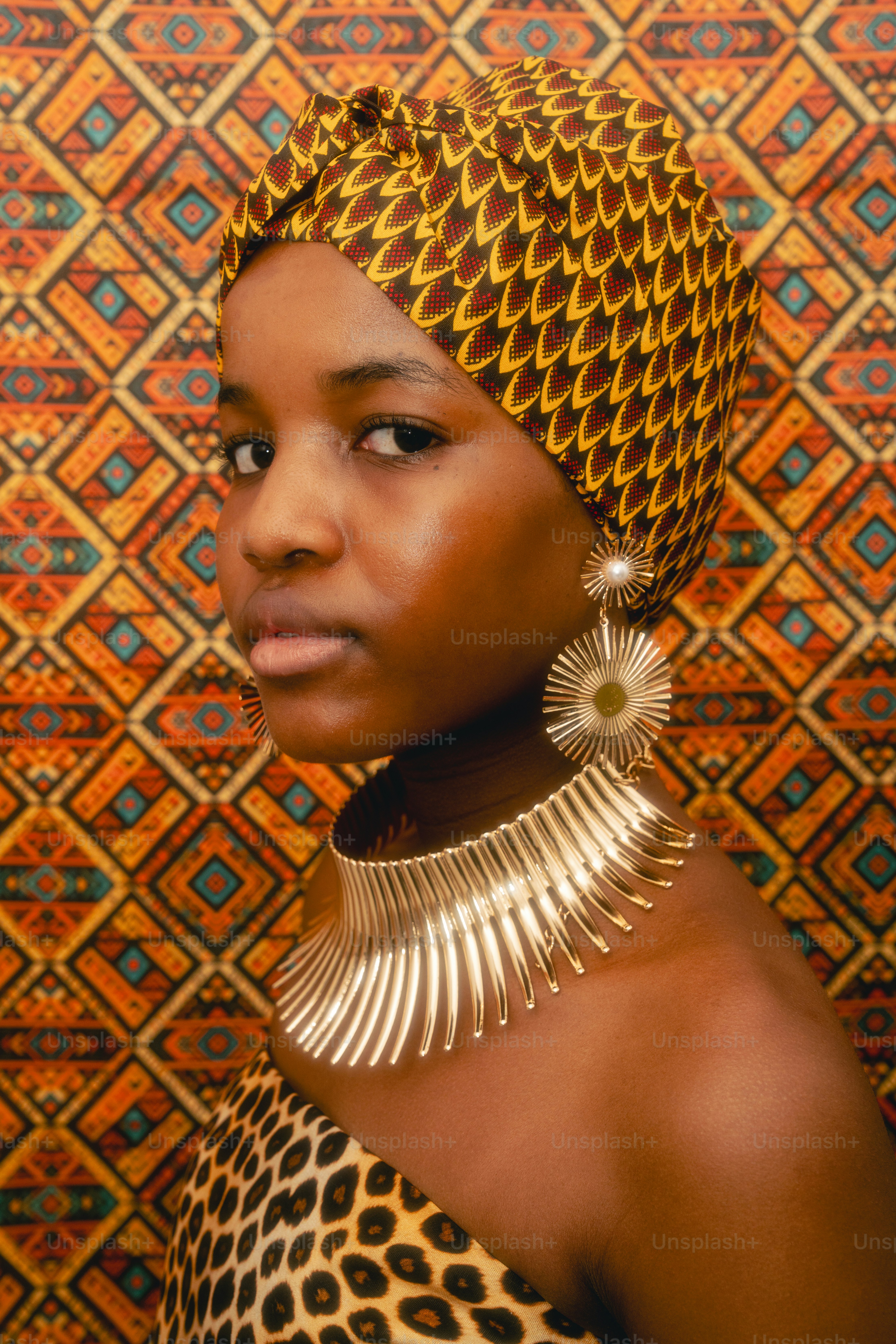 Woman with patterned headwrap, gold jewelry, and patterned background