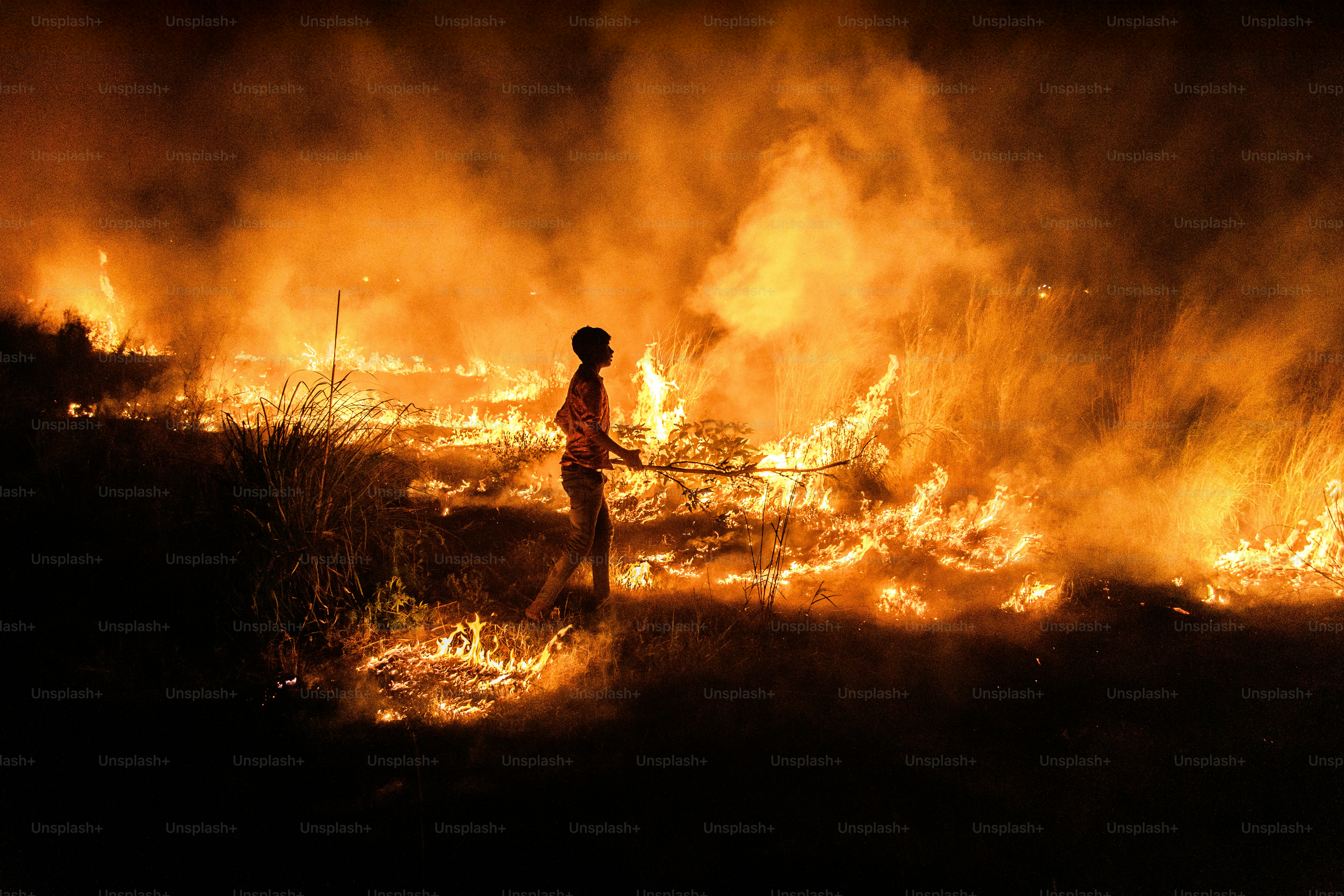 A person walks through a field of fire at night.