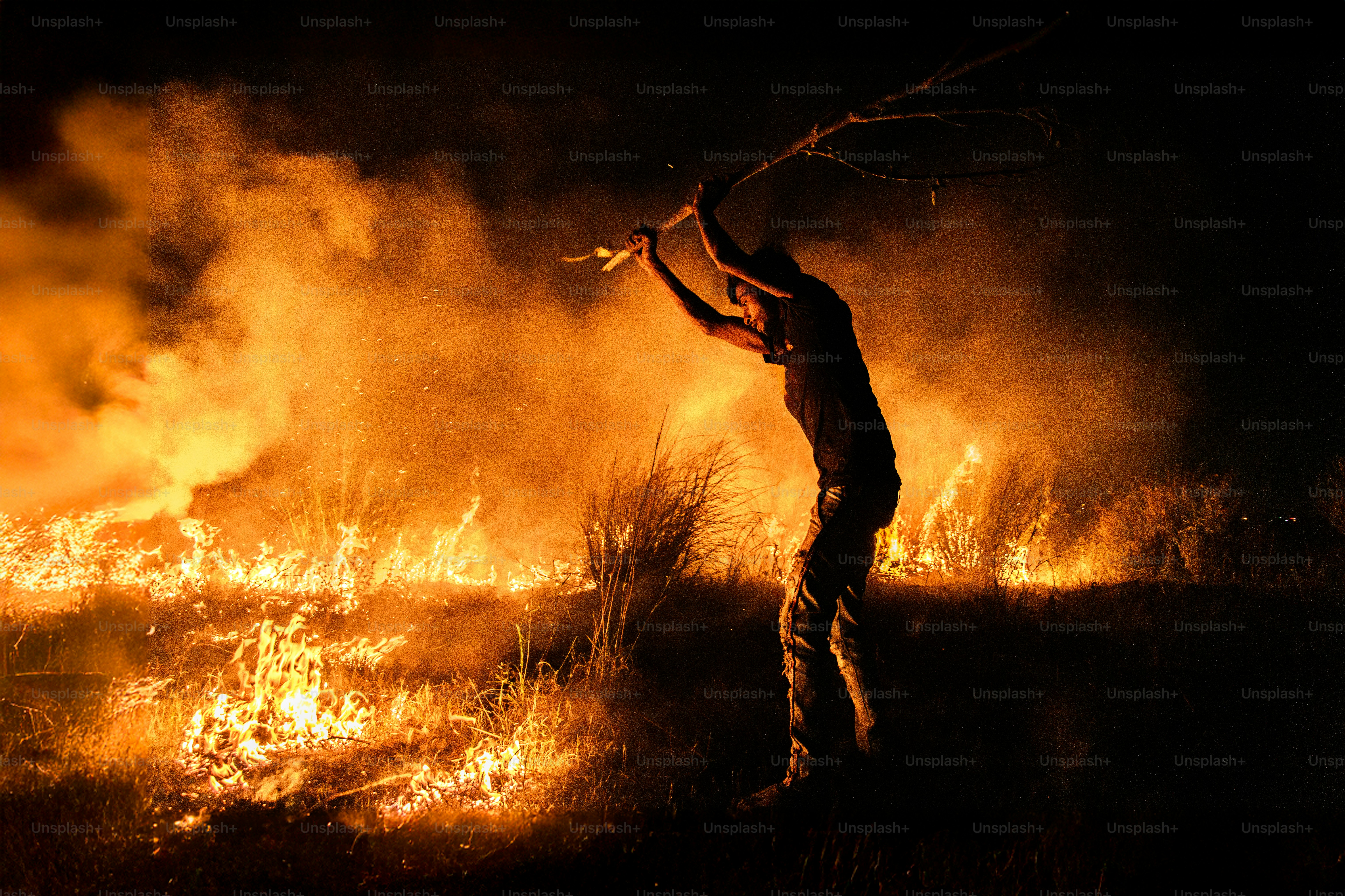 Person with stick in front of large grass fire