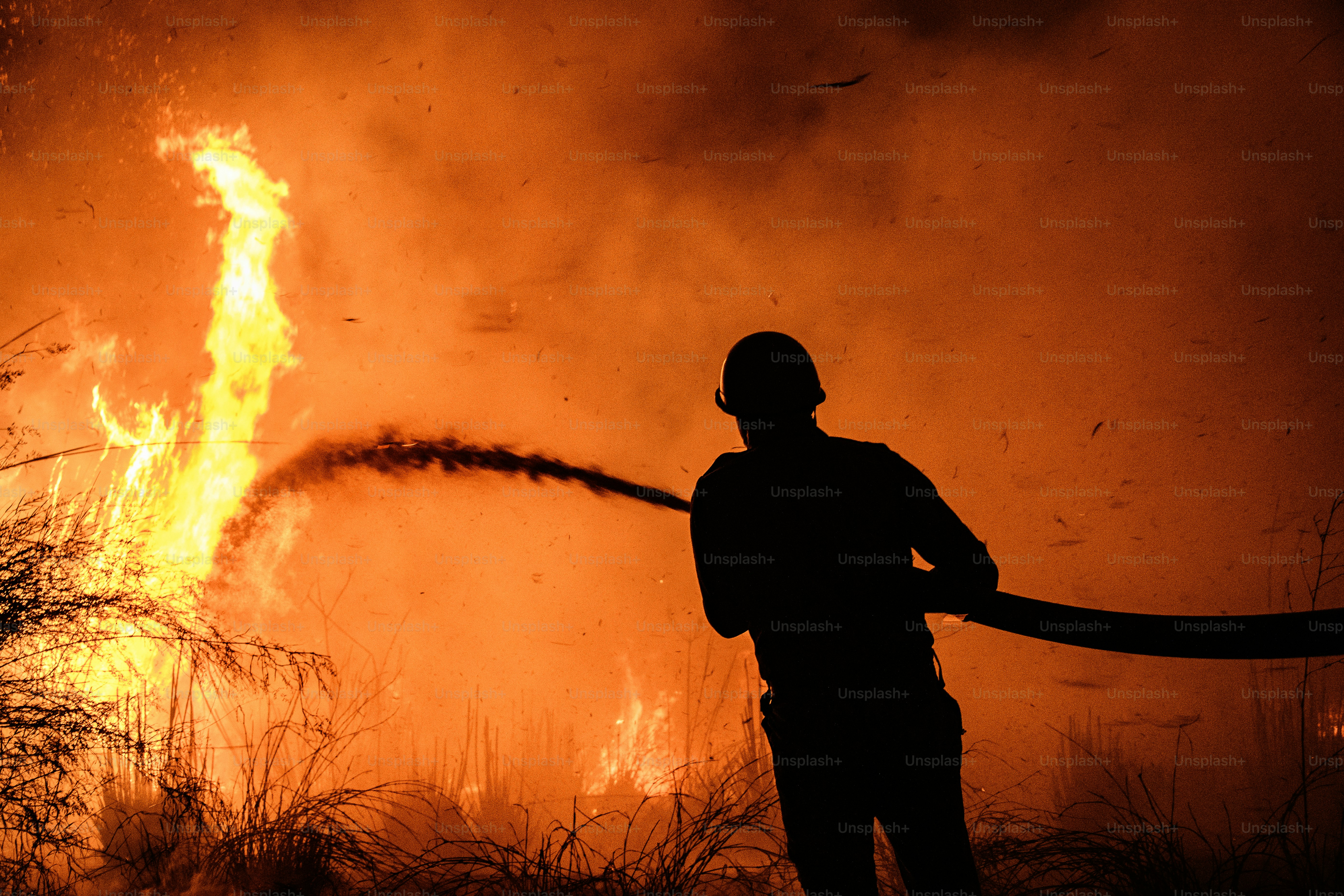 Firefighter sprays water on a raging wildfire at night