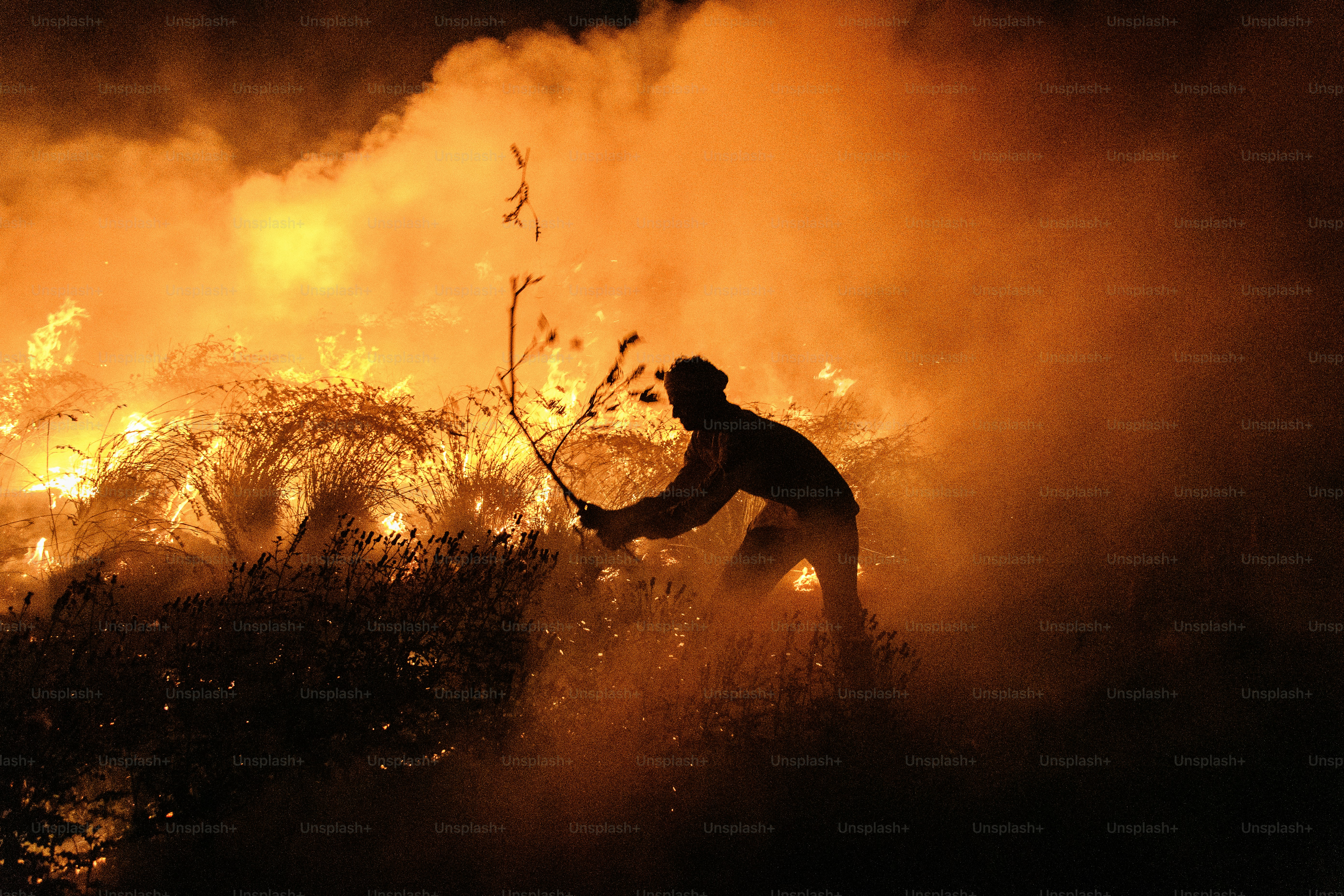 Person battling a large, intense wildfire at night