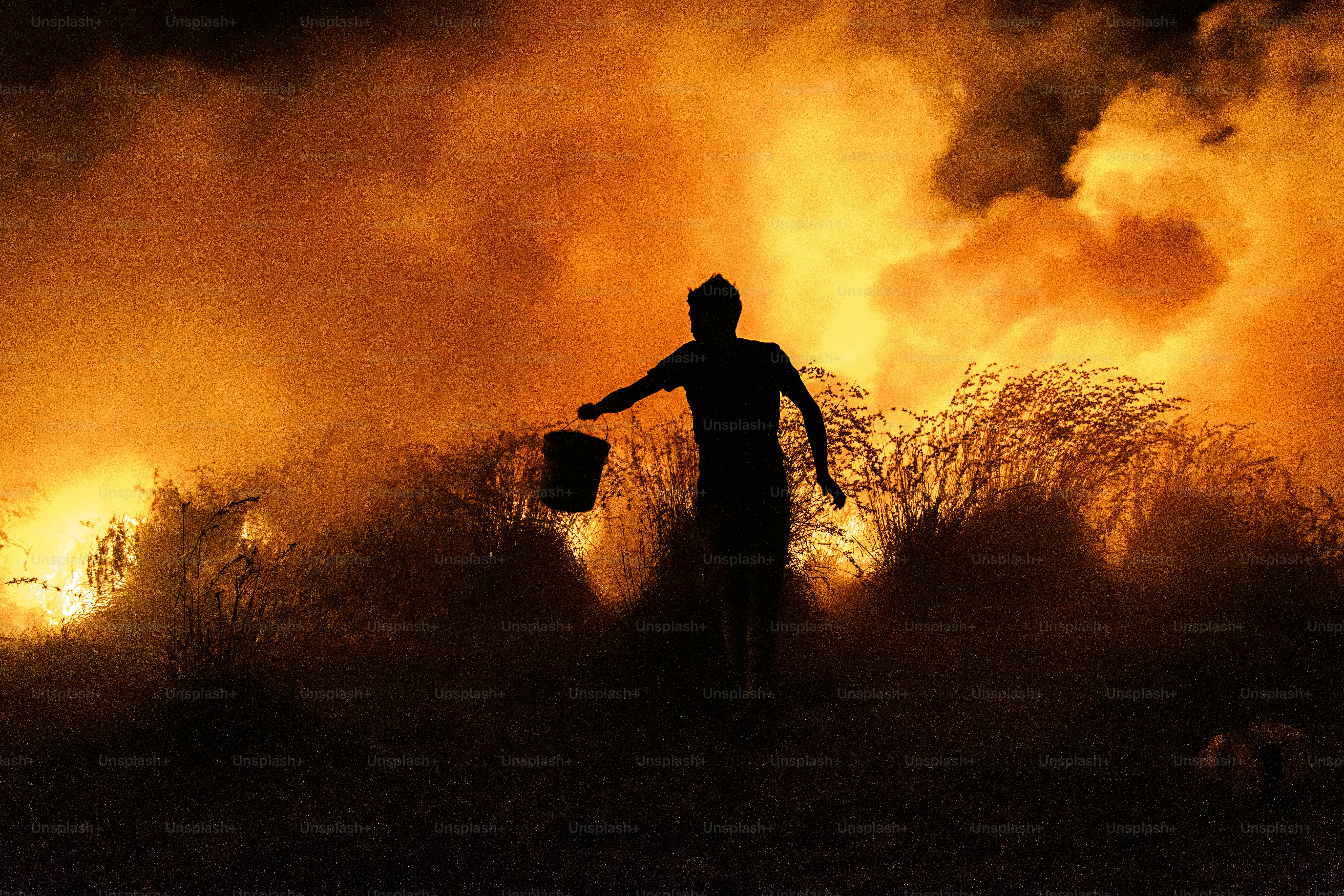 Silhouette of a person carrying a bucket amidst flames