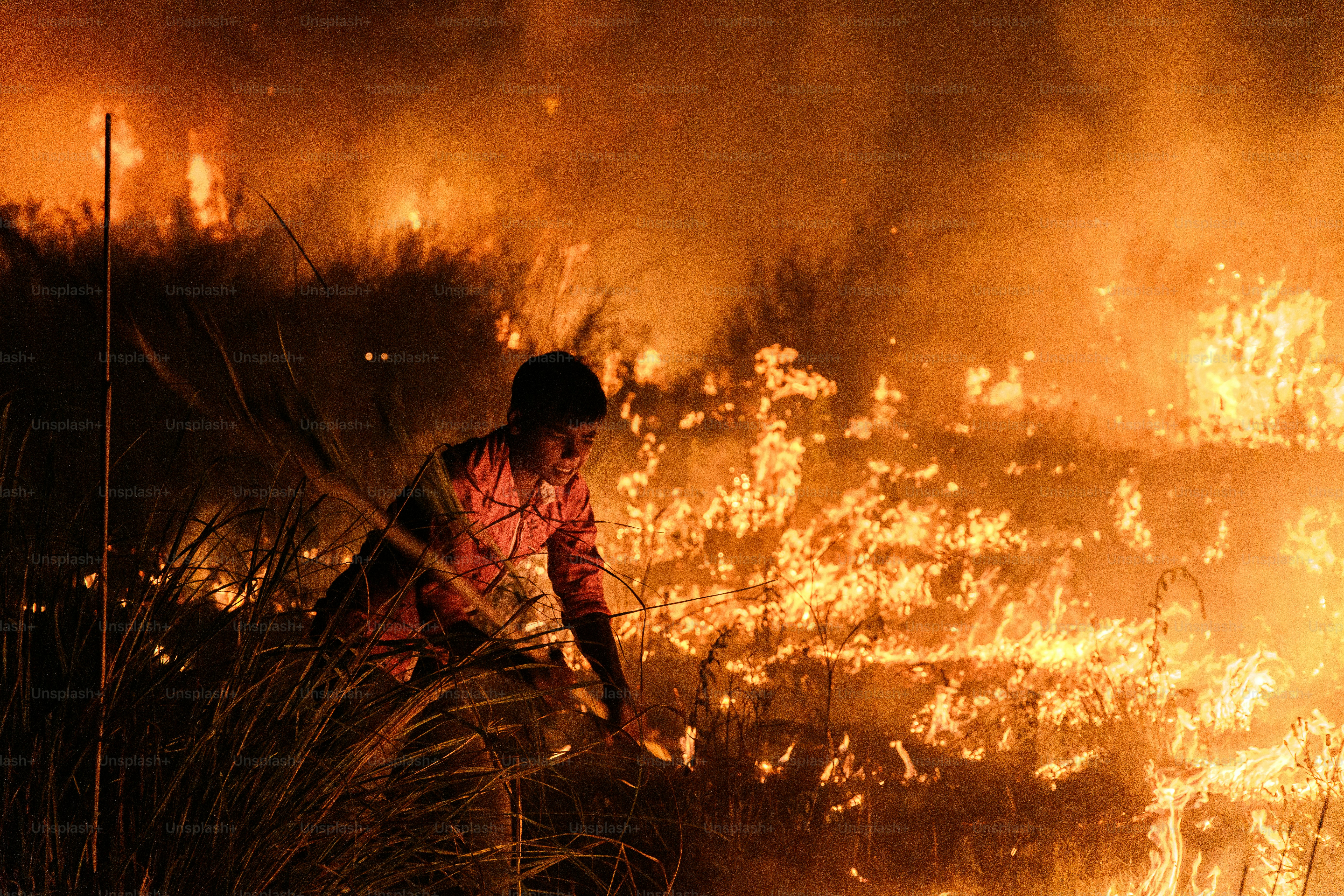 A person walks through a field of burning grass.