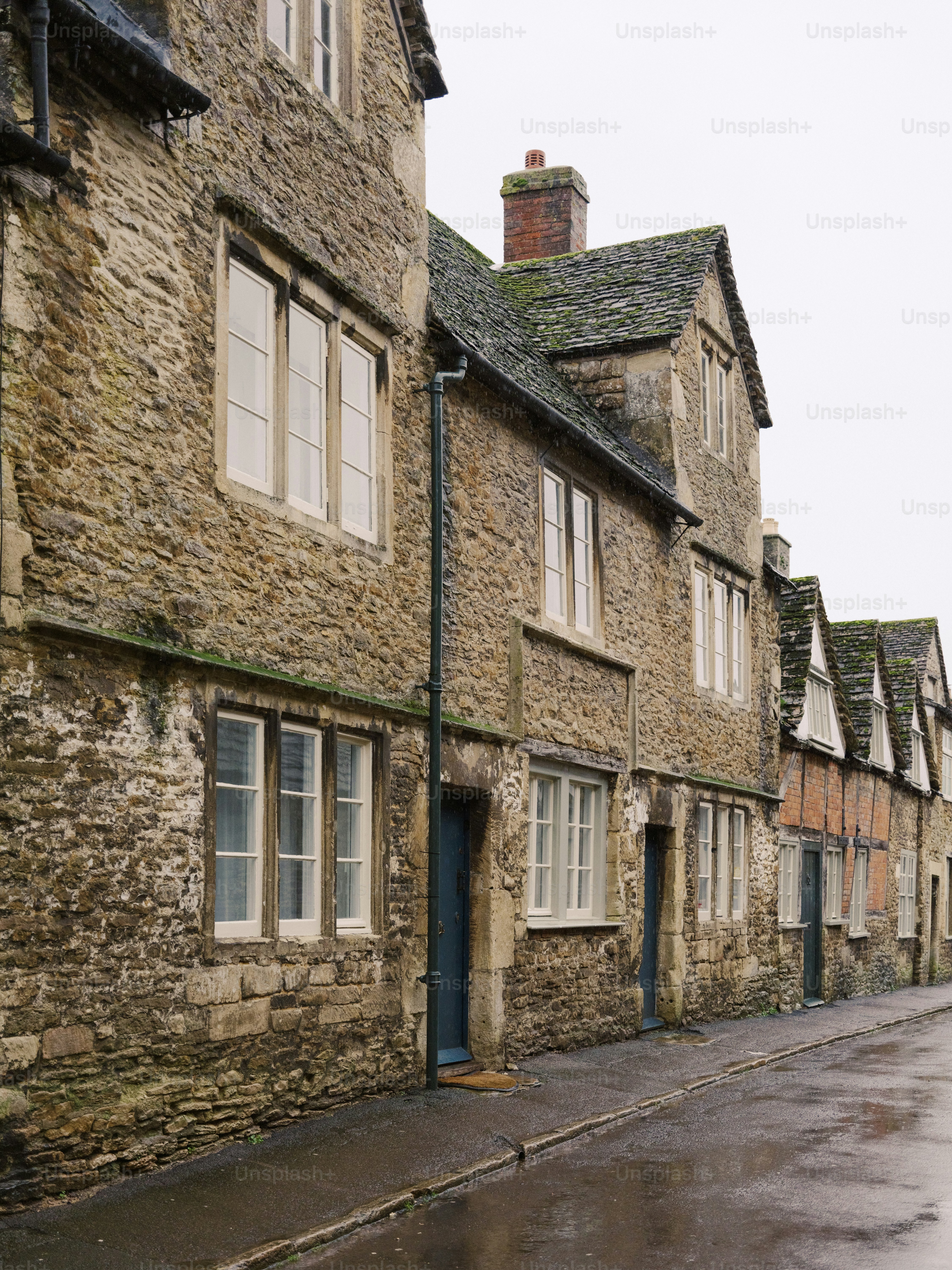 Old stone houses line a wet cobblestone street.