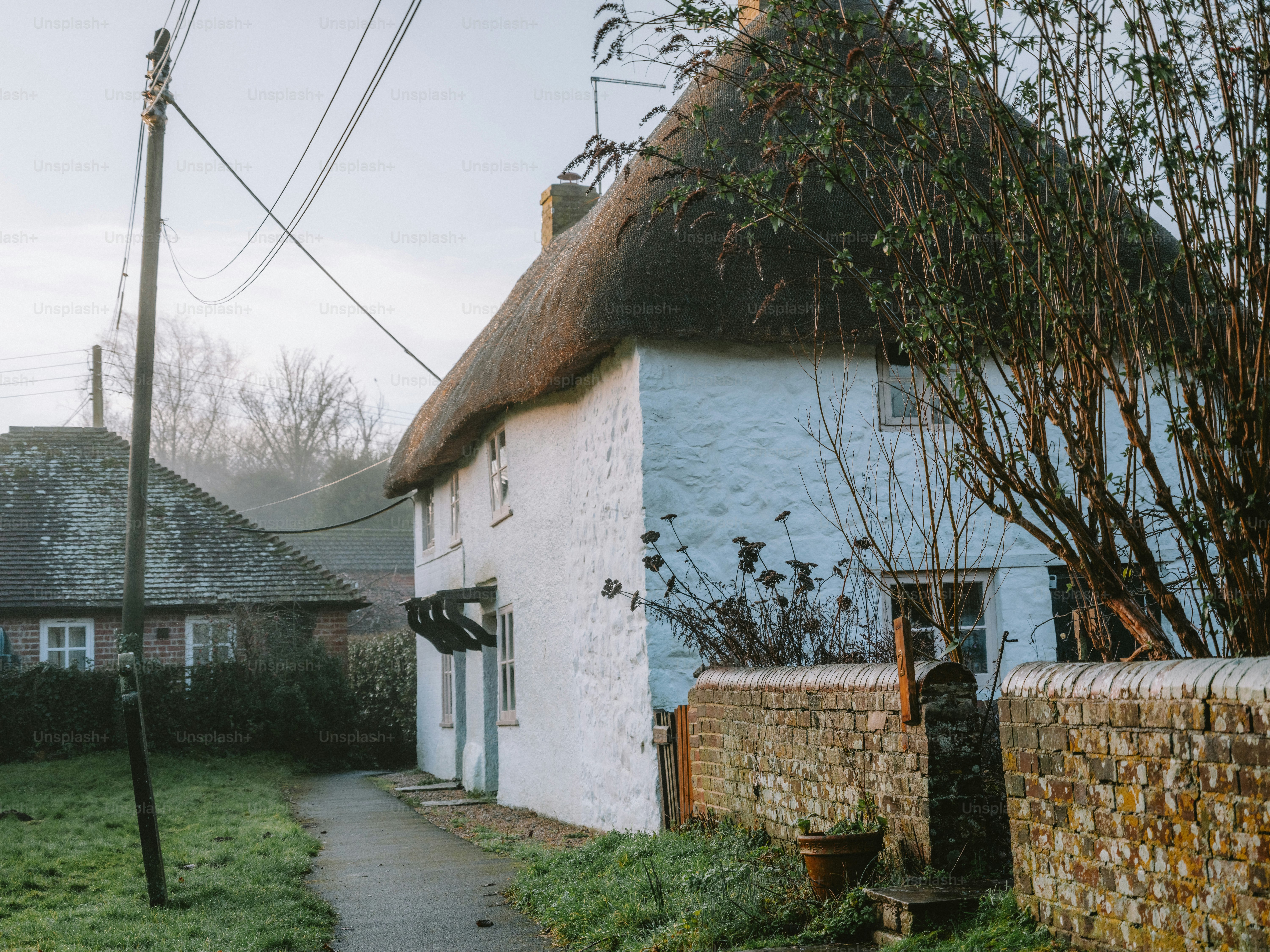 White cottage with thatched roof and stone wall.