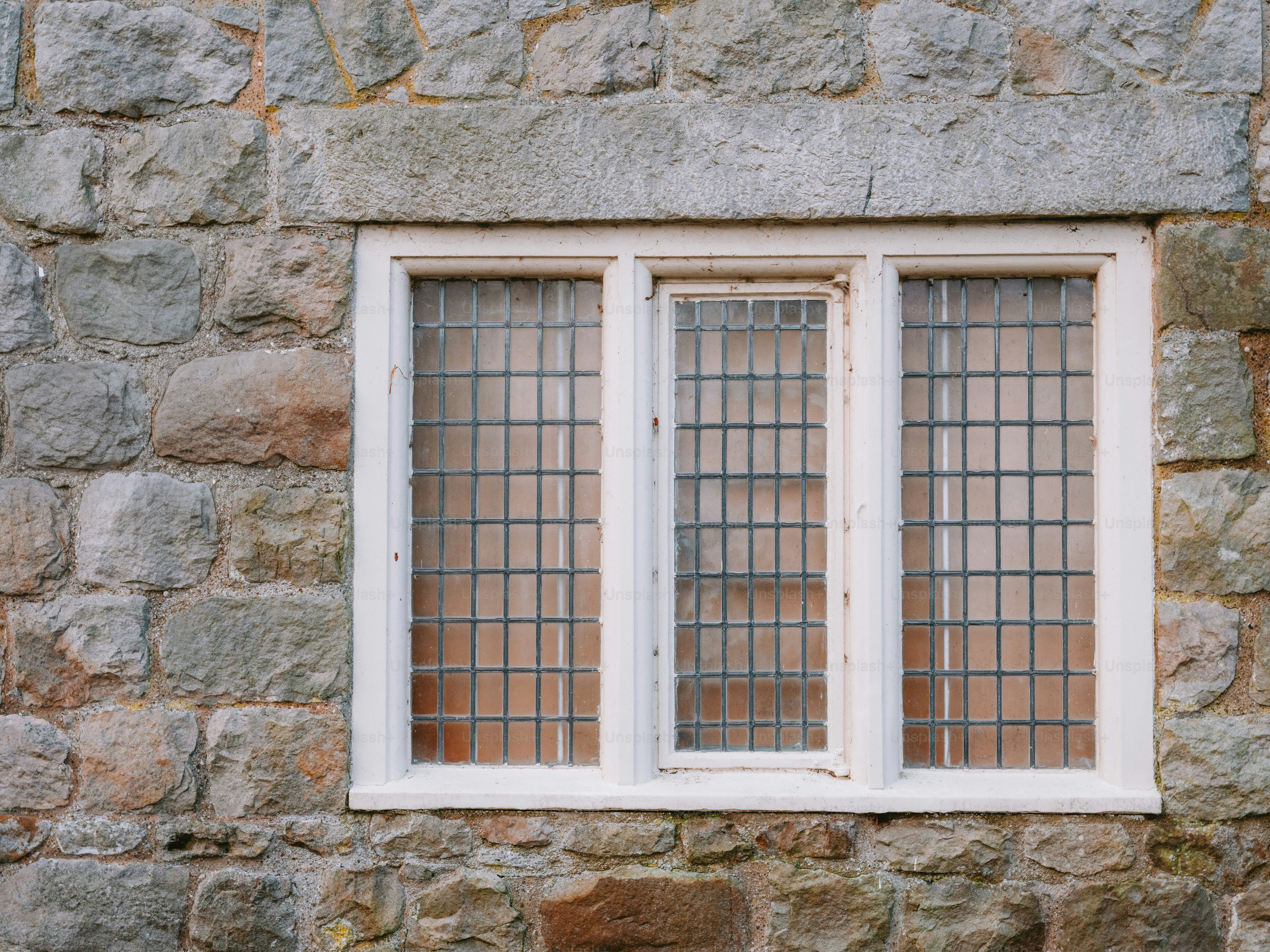 A white-framed window with three panes on a stone wall