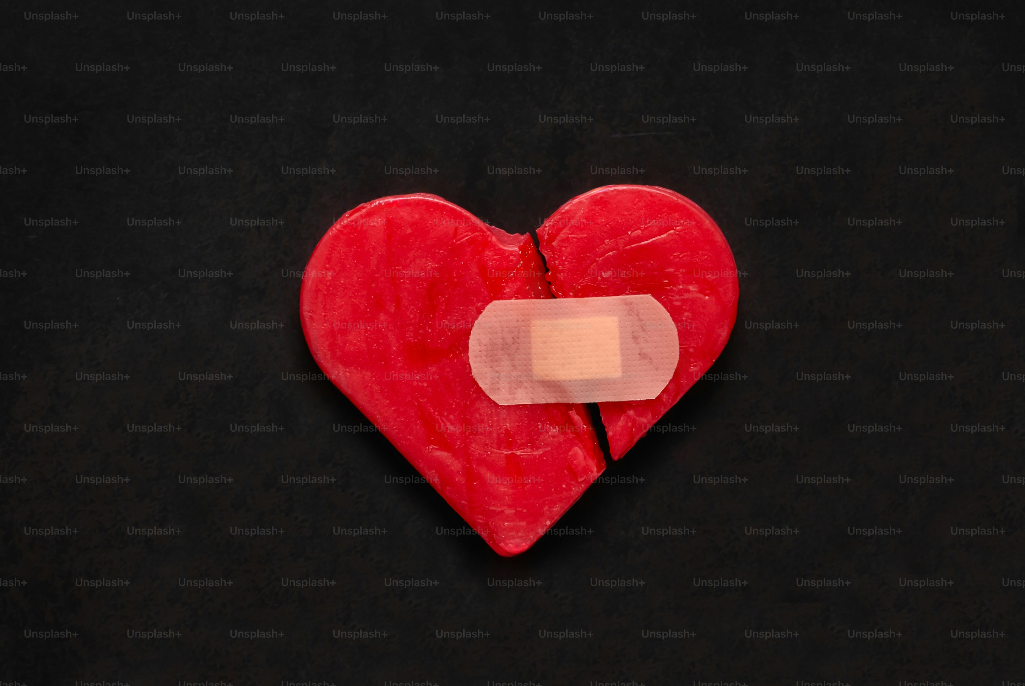 A cracked red heart with a bandage on it.