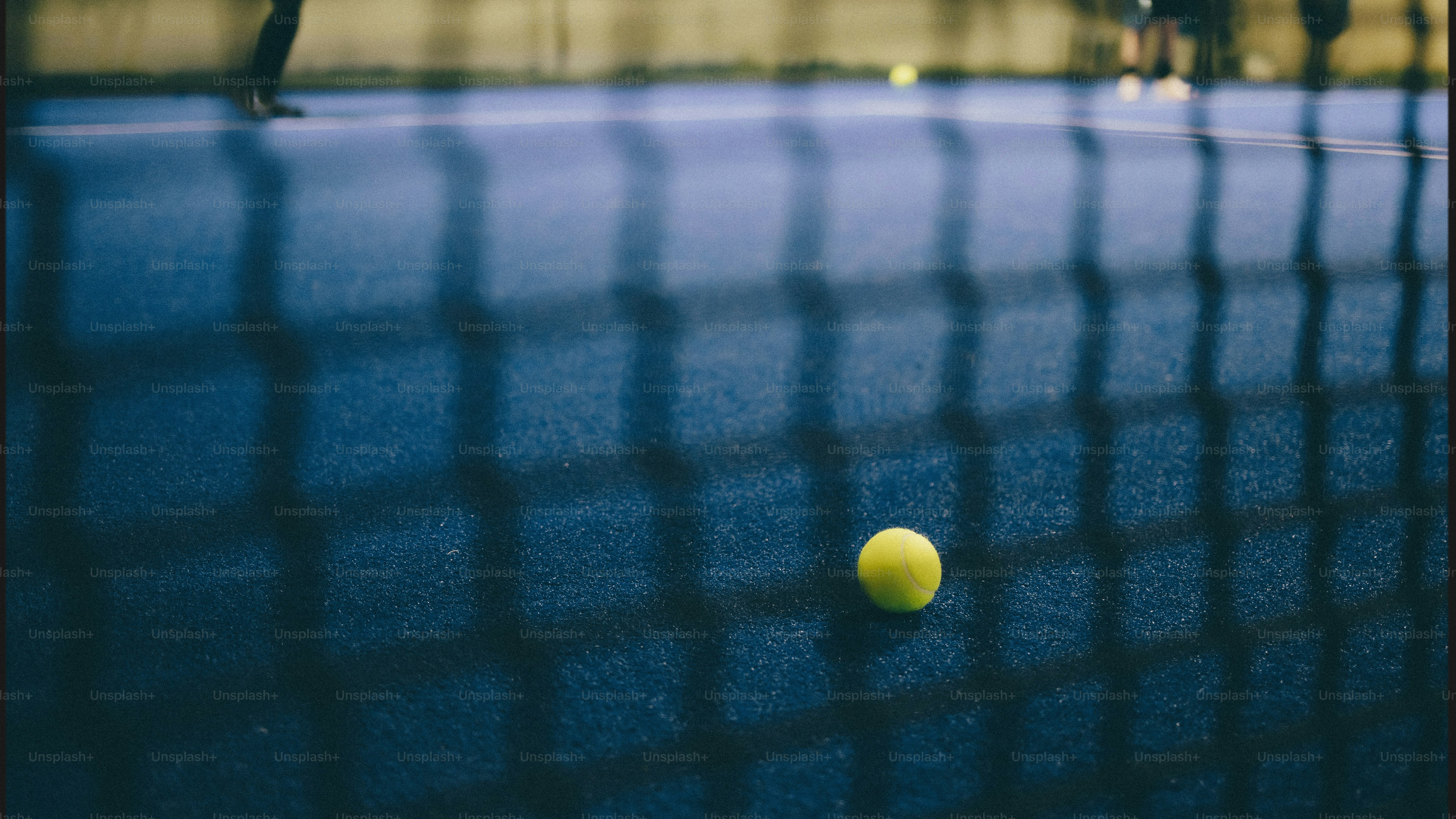 Ein gelber Ball auf einem blauen Platz durch ein Netz