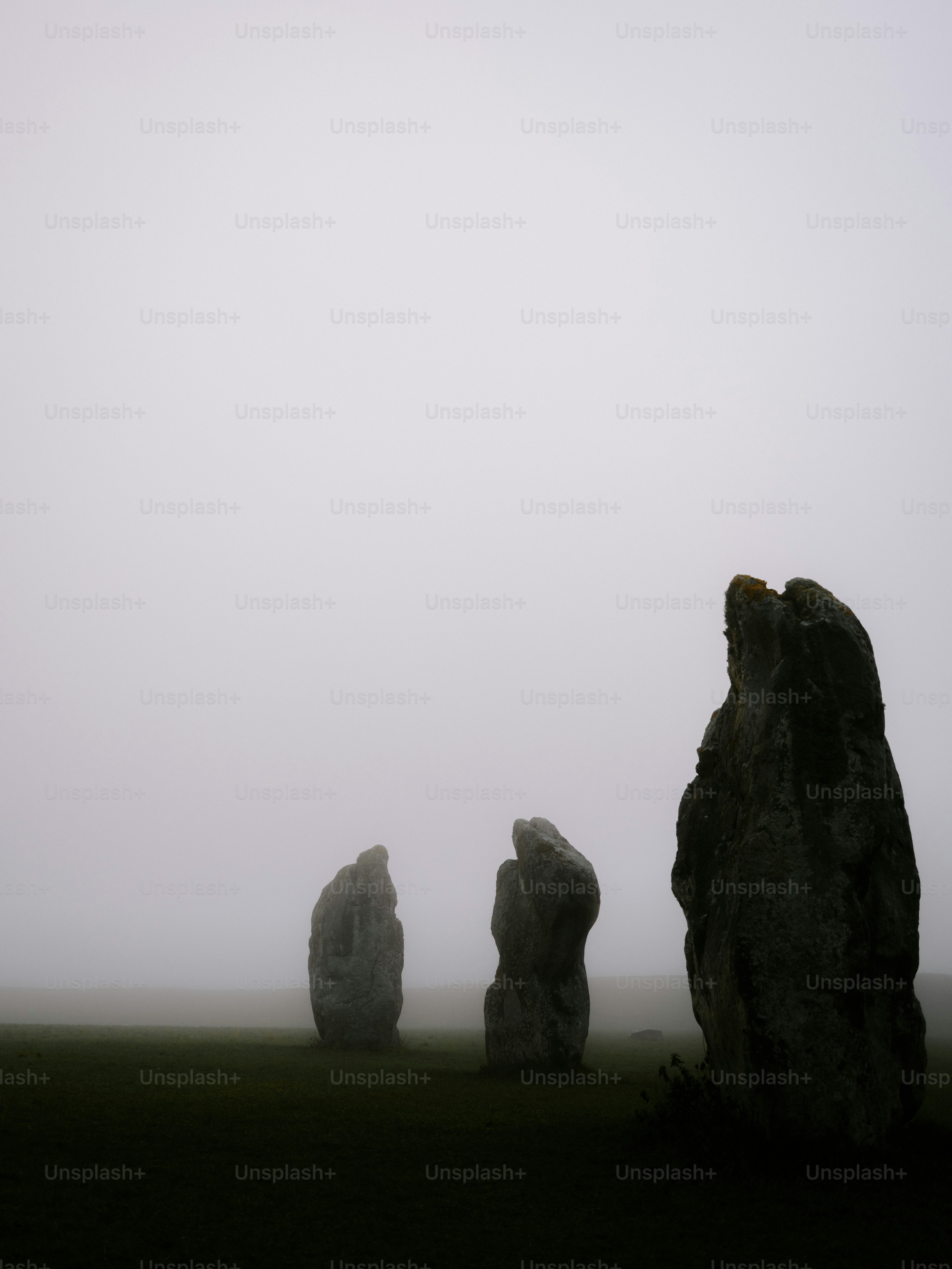 Megalithic stones stand in a misty field.