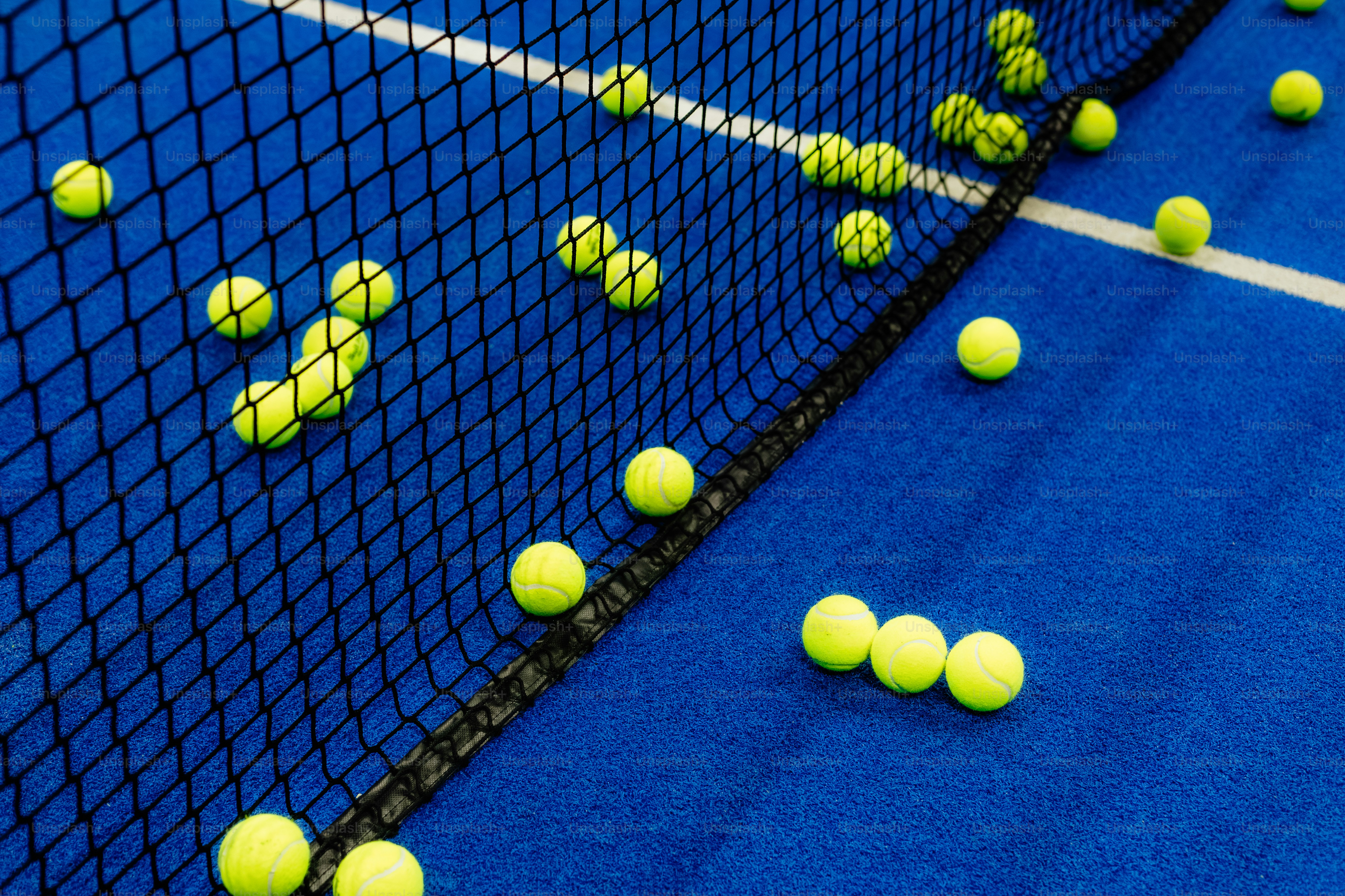Tennis balls scattered on a blue court near net