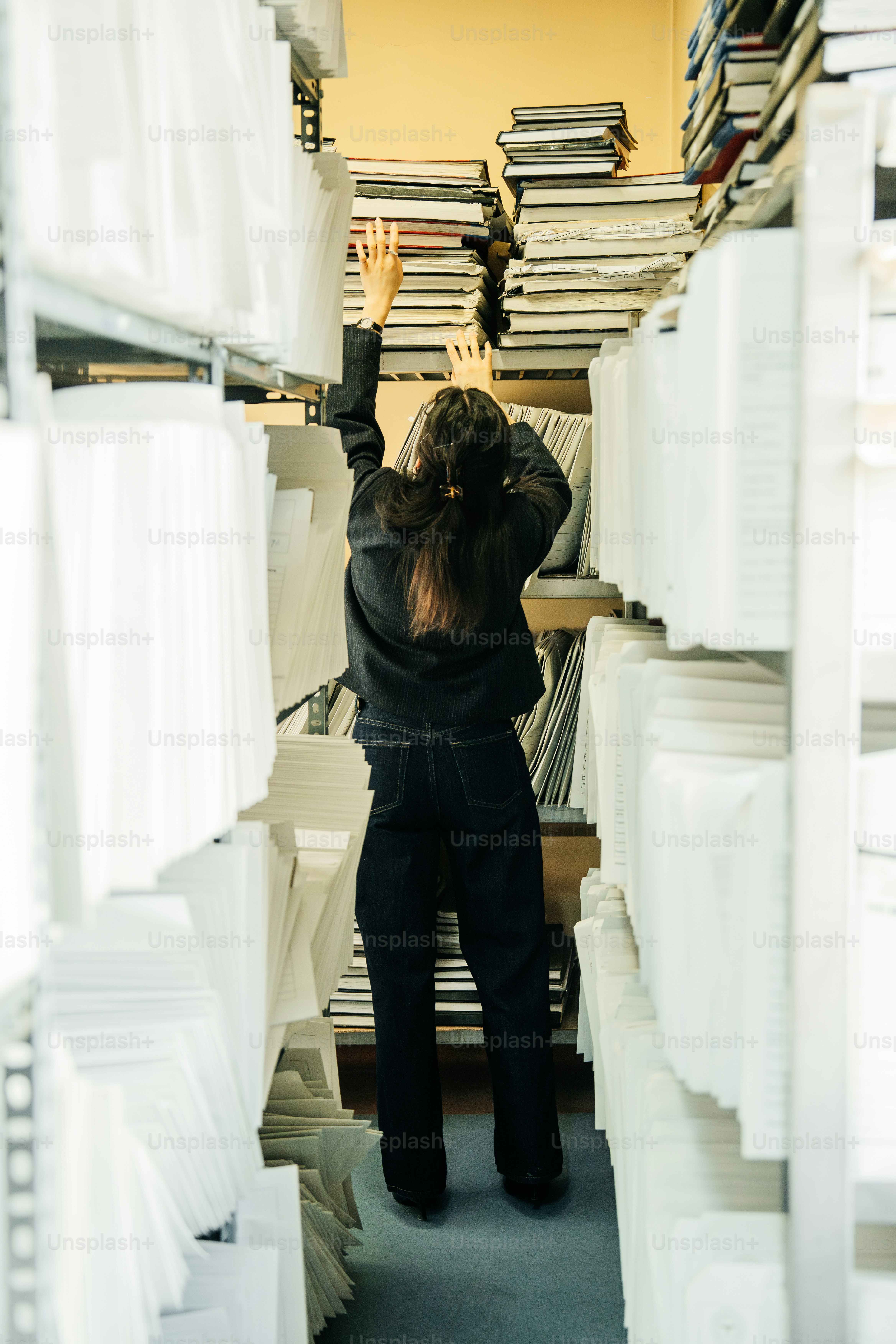 A person reaching for books on a tall shelf.