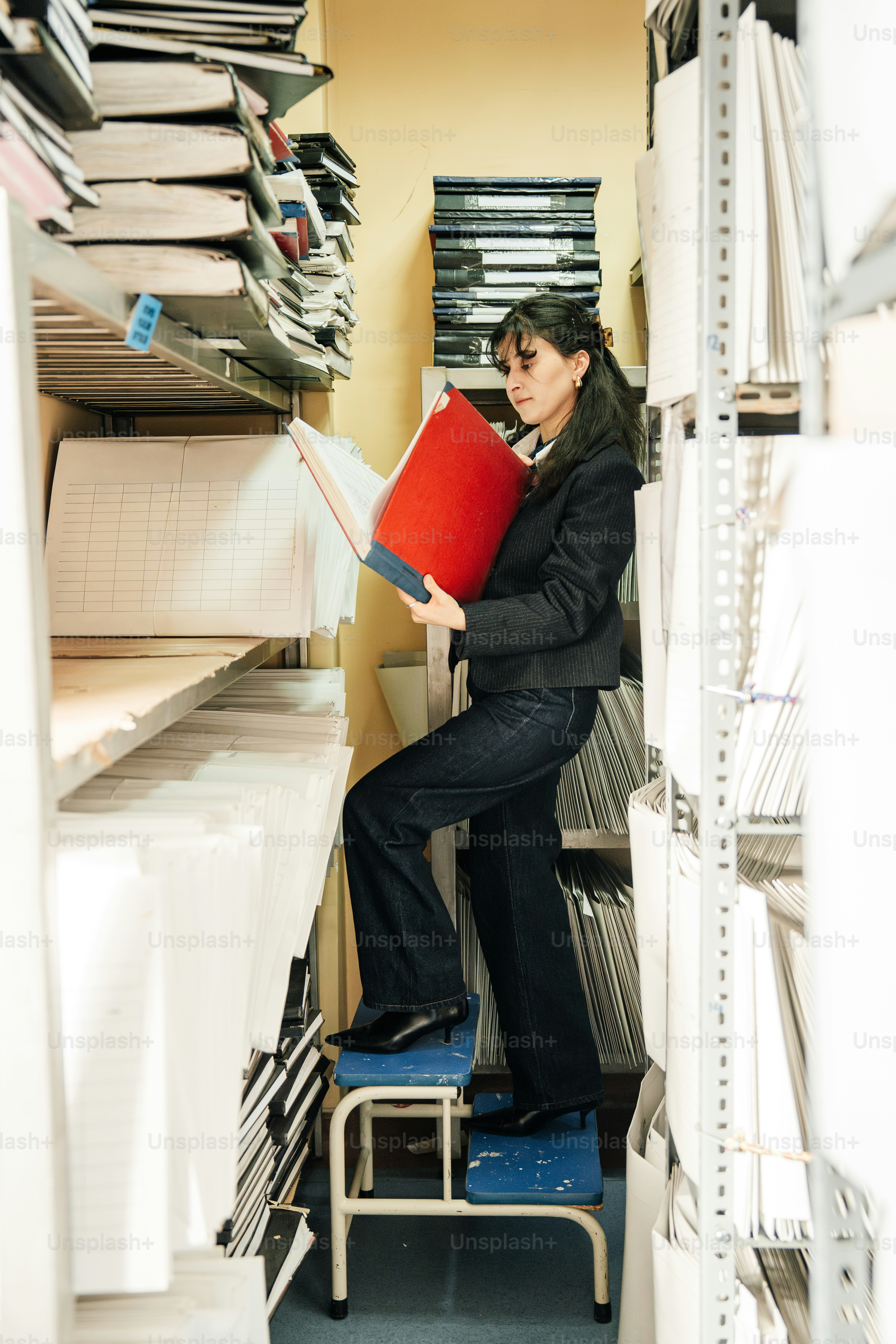 Woman standing on stepladder reaching for document