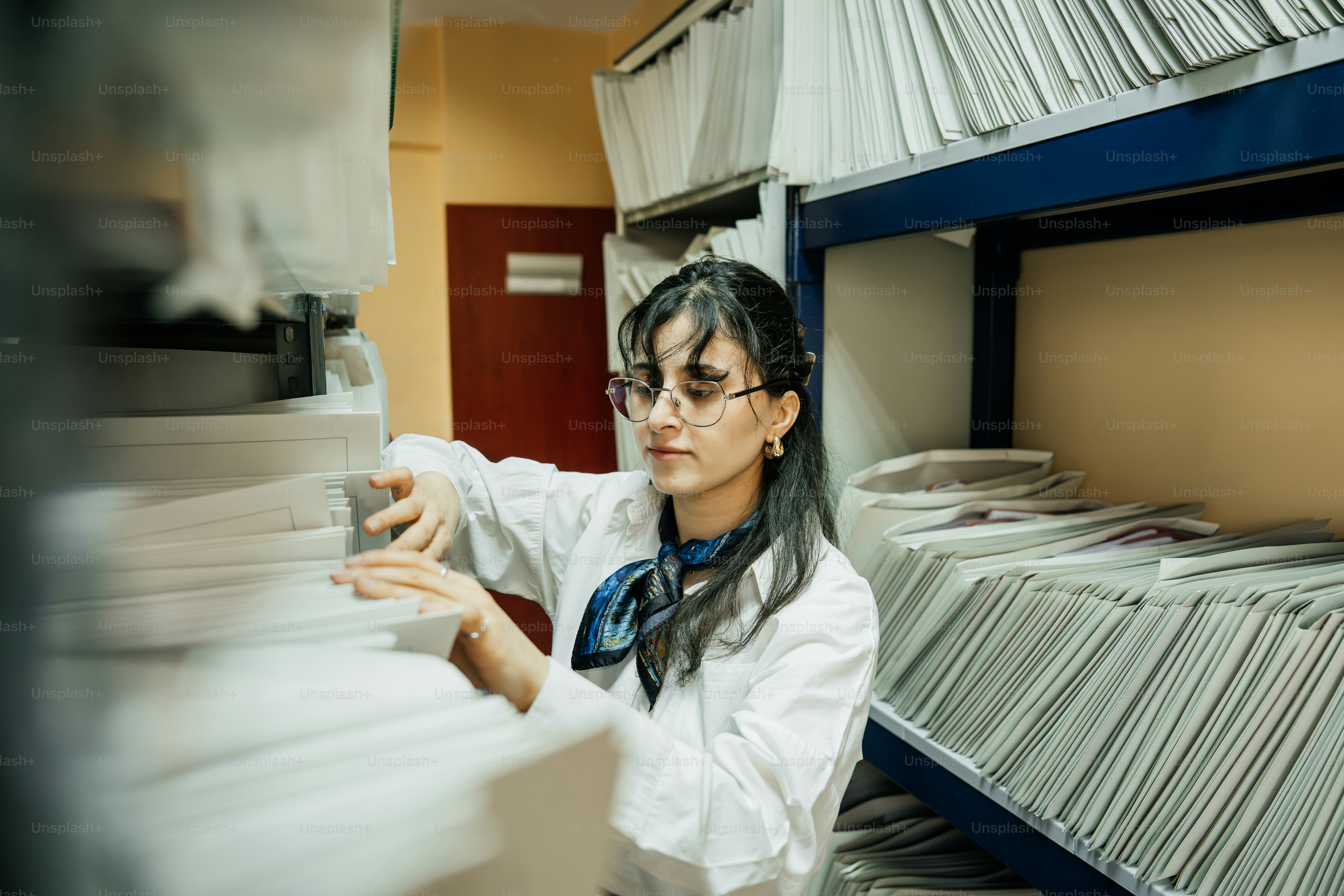 Woman in lab coat sorts through files in archive