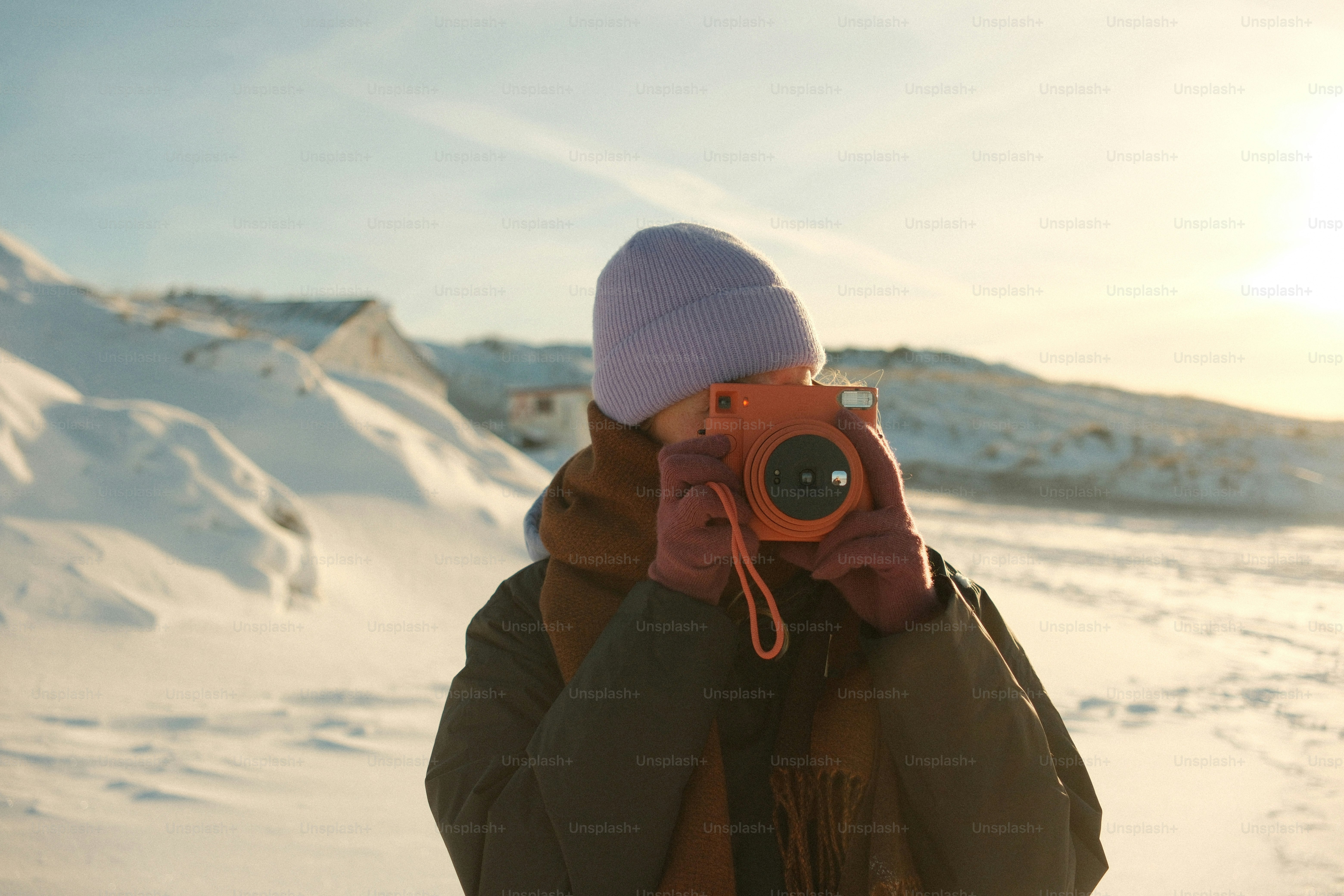 Person holding an orange instant camera in snowy landscape
