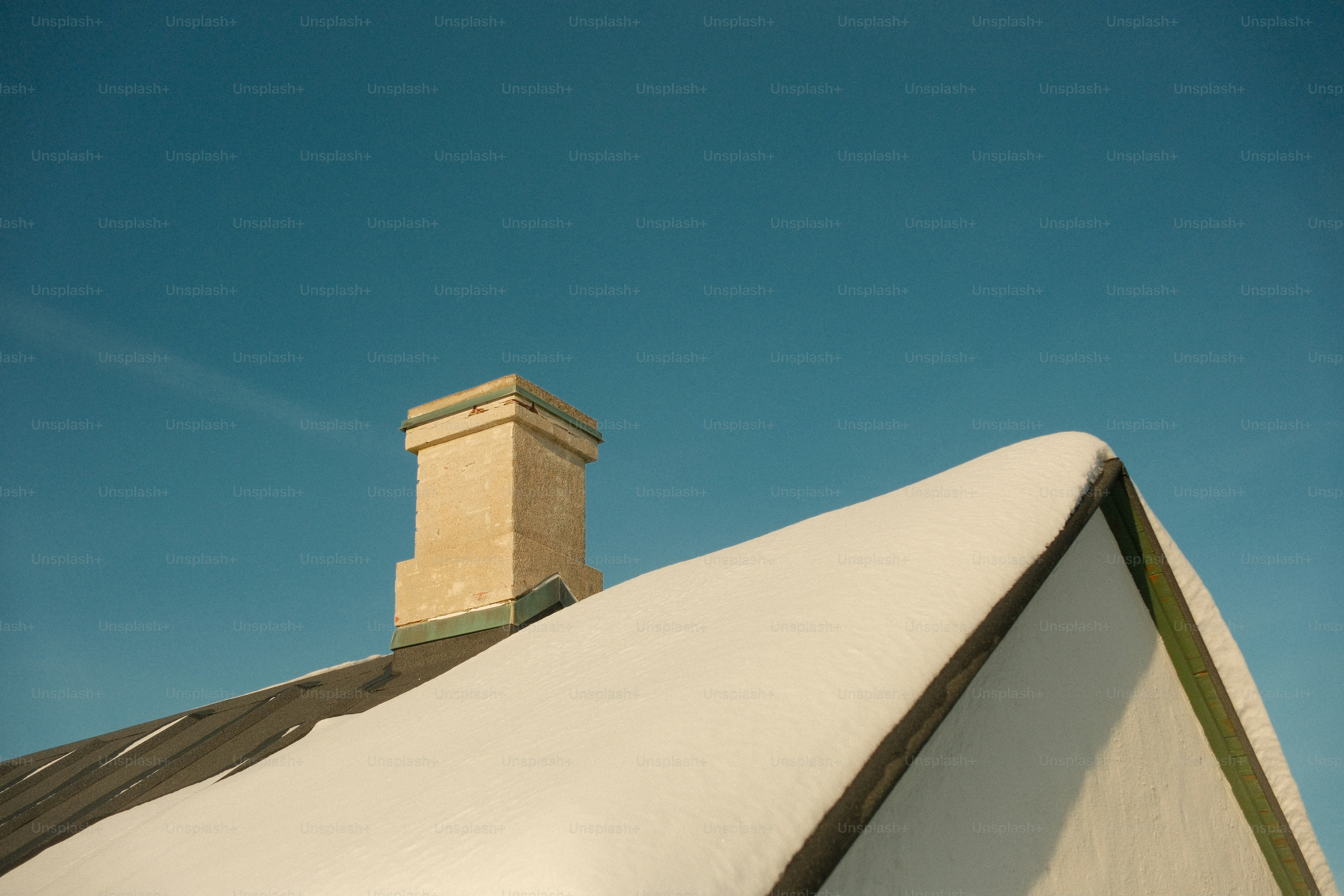 Snow covered roof with chimney against blue sky