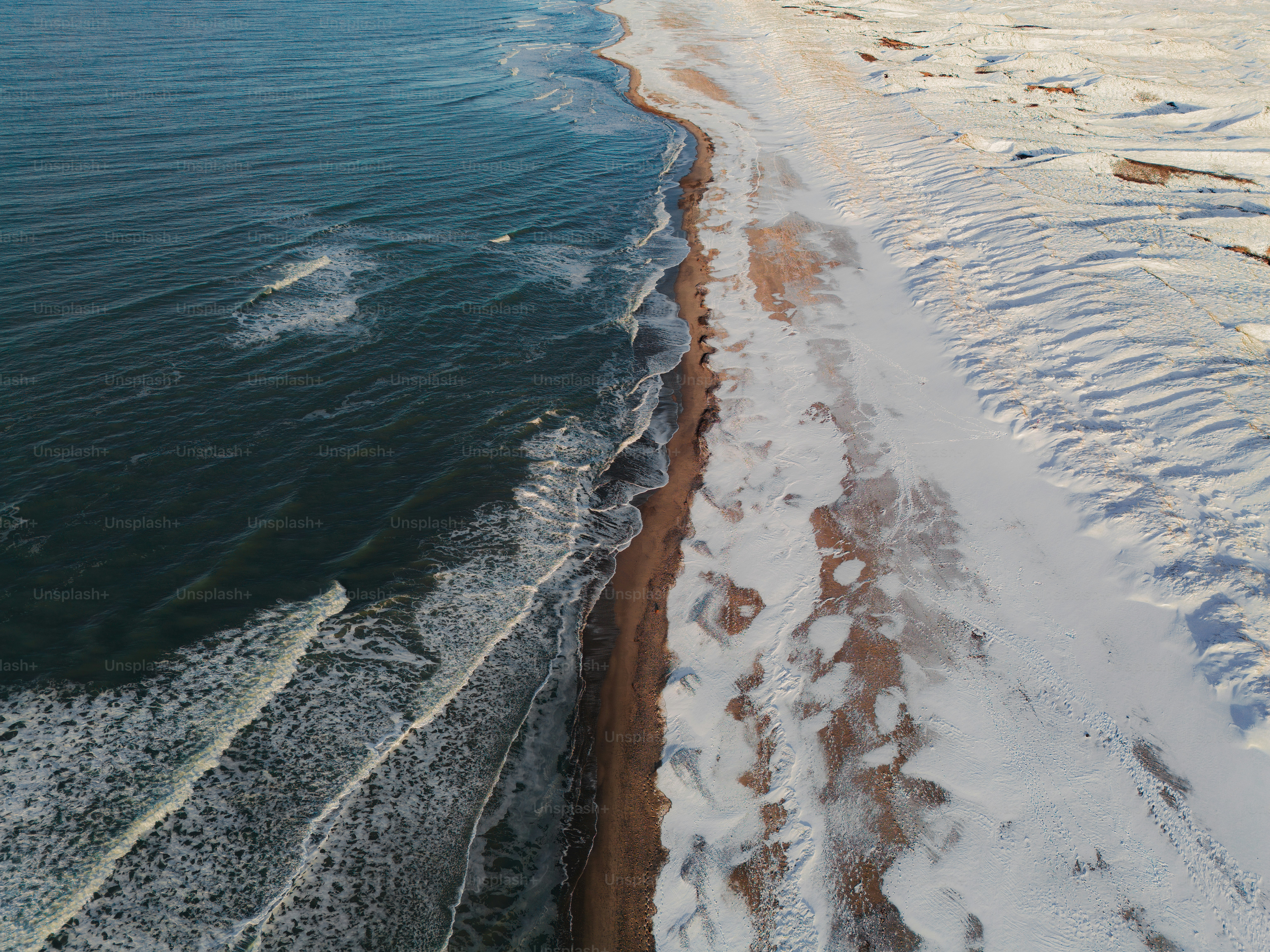 Les vagues lègnent doucement une plage enneigée en hiver.