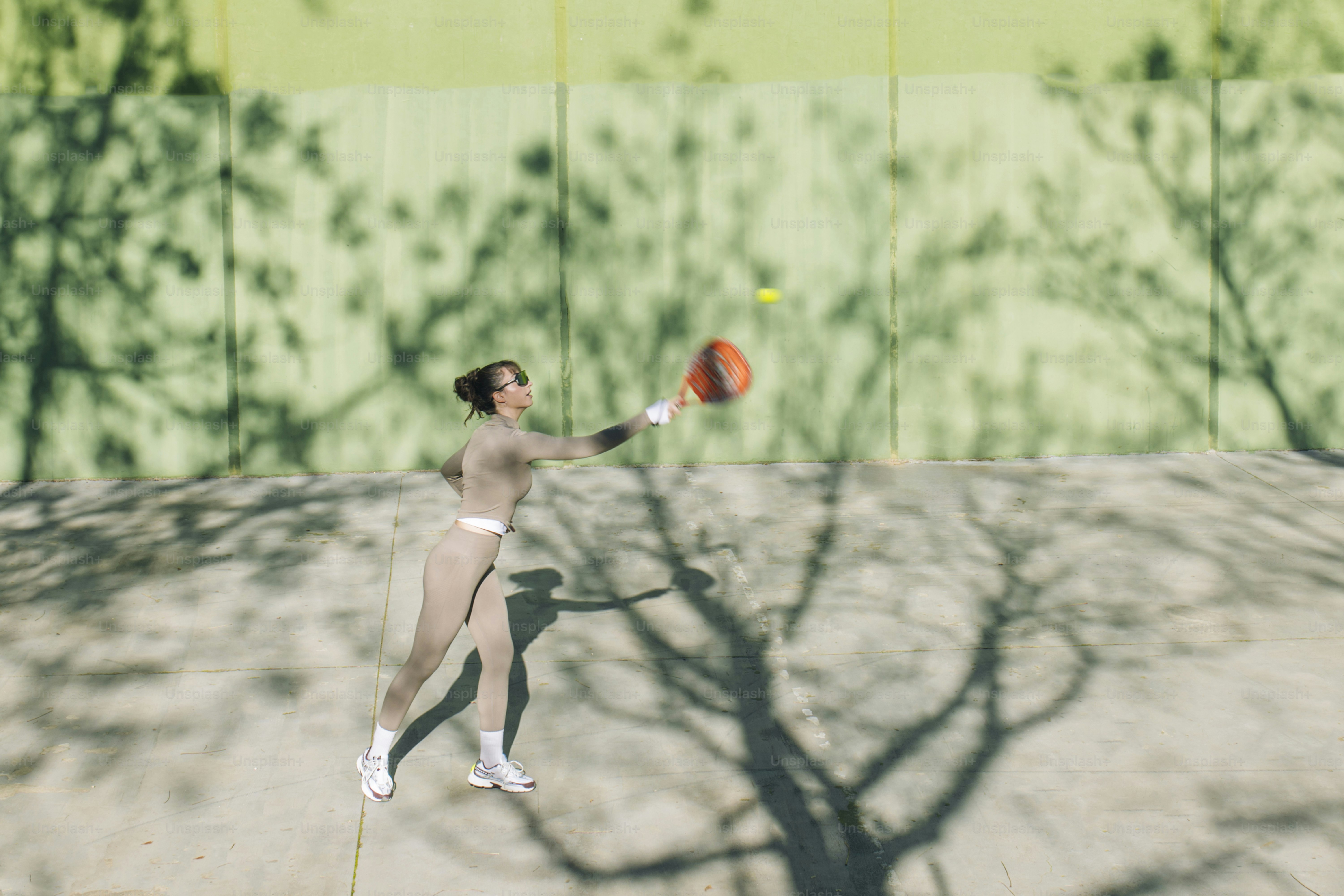 Frau spielt Tennis vor einem Schattenhintergrund eines Baumes