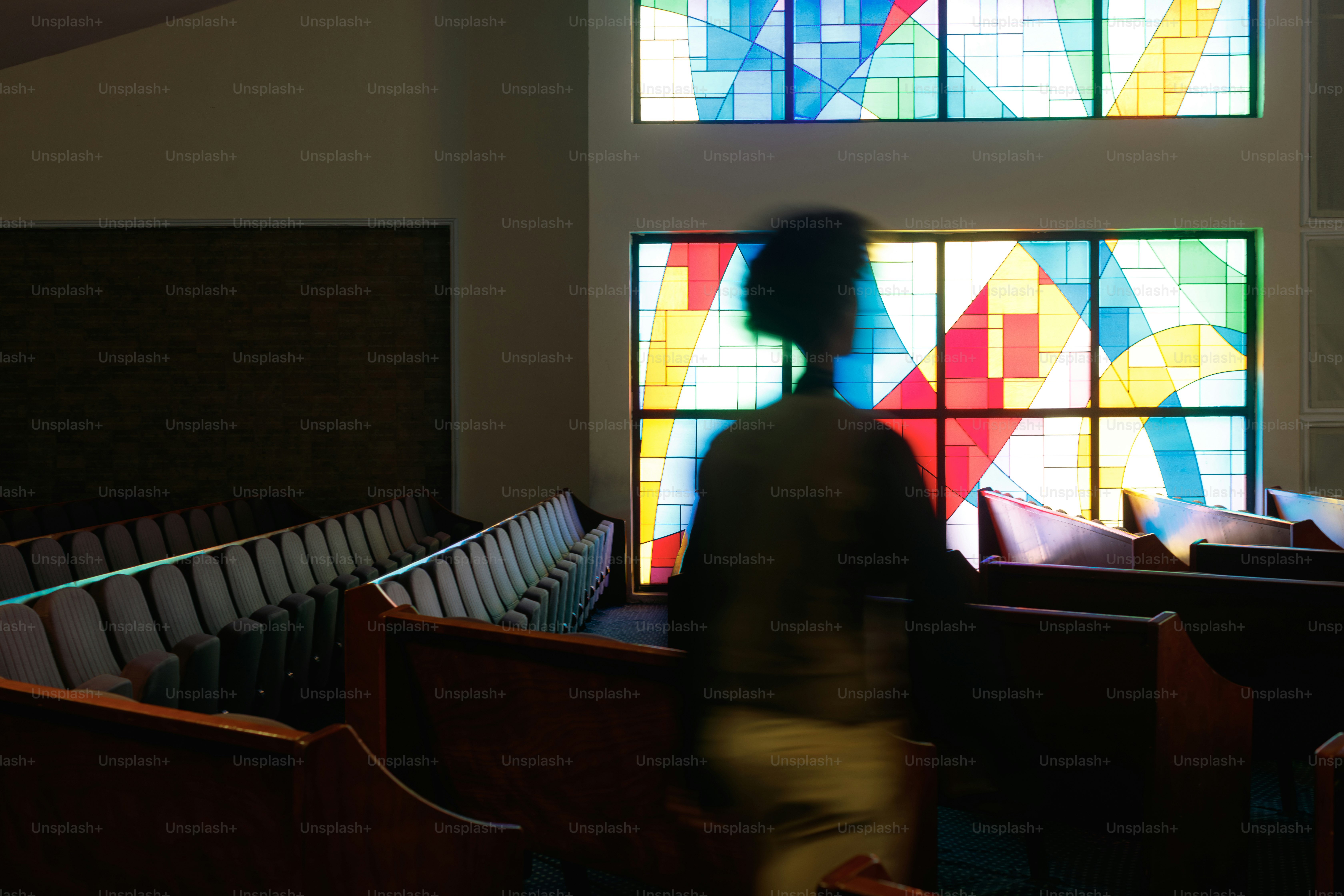 教会のステンドグラスの窓の前を歩く人物