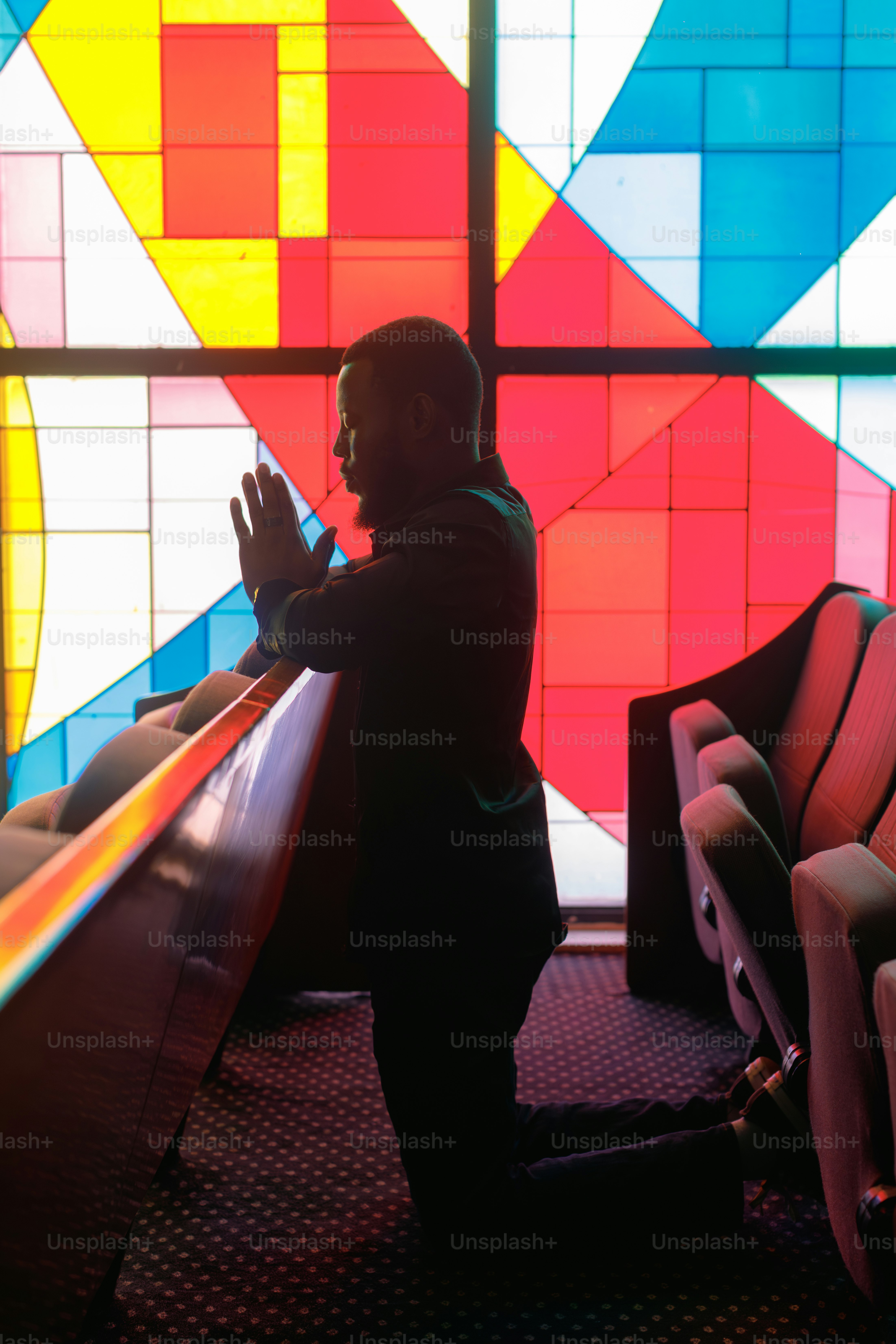 Man praying on knees before colorful stained glass window