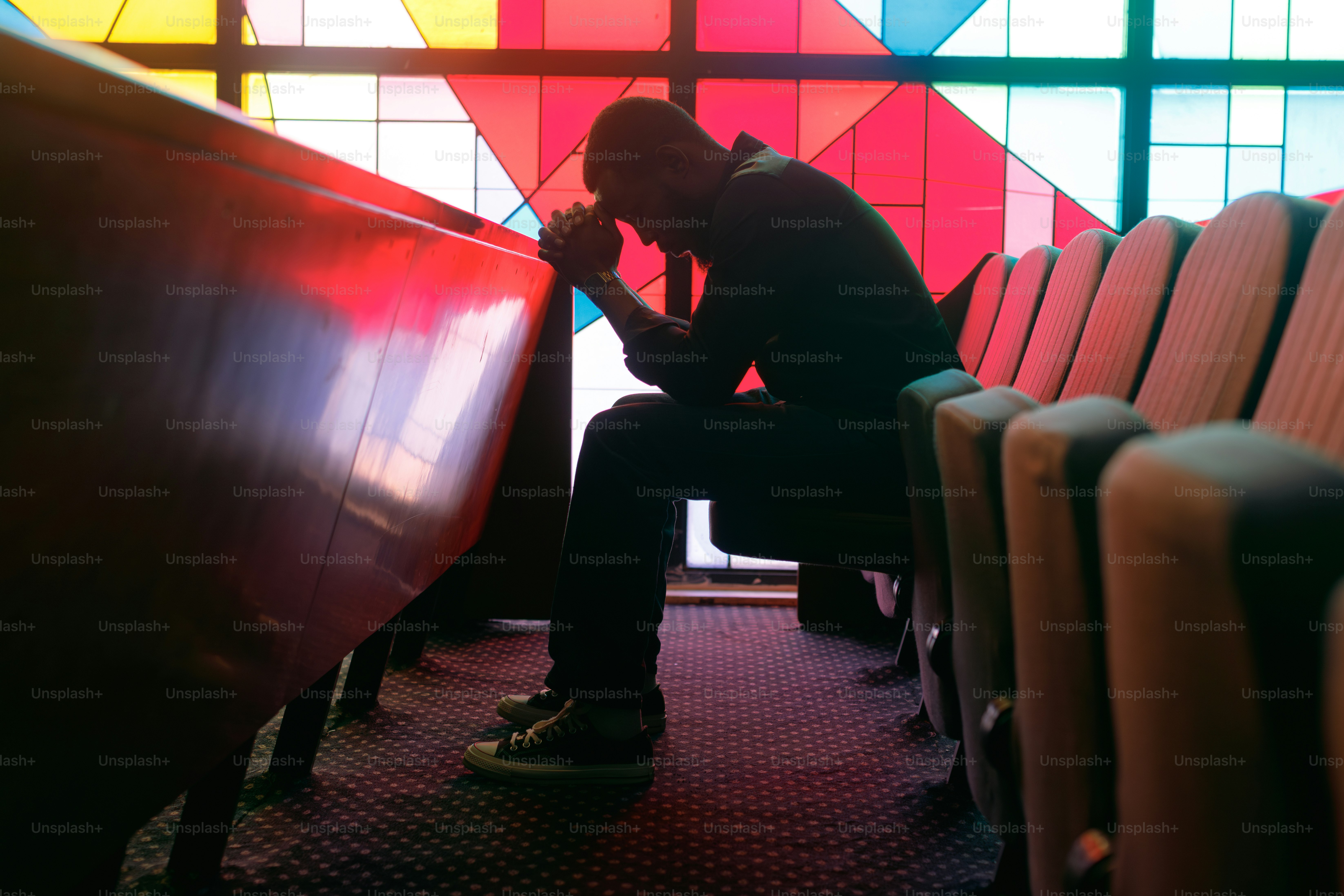 Man praying in a church pew with stained glass window
