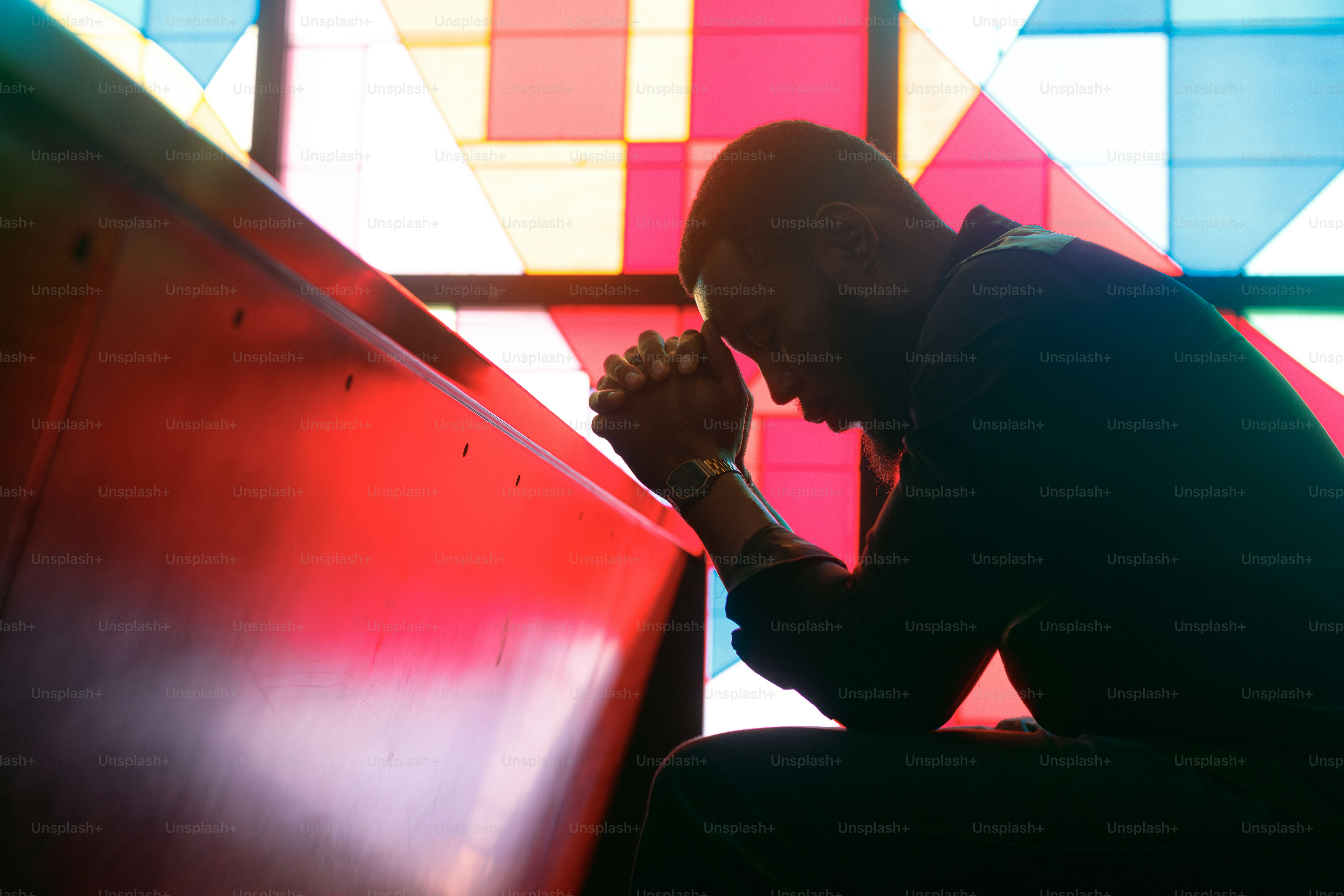 Man praying in a church pew with stained glass.