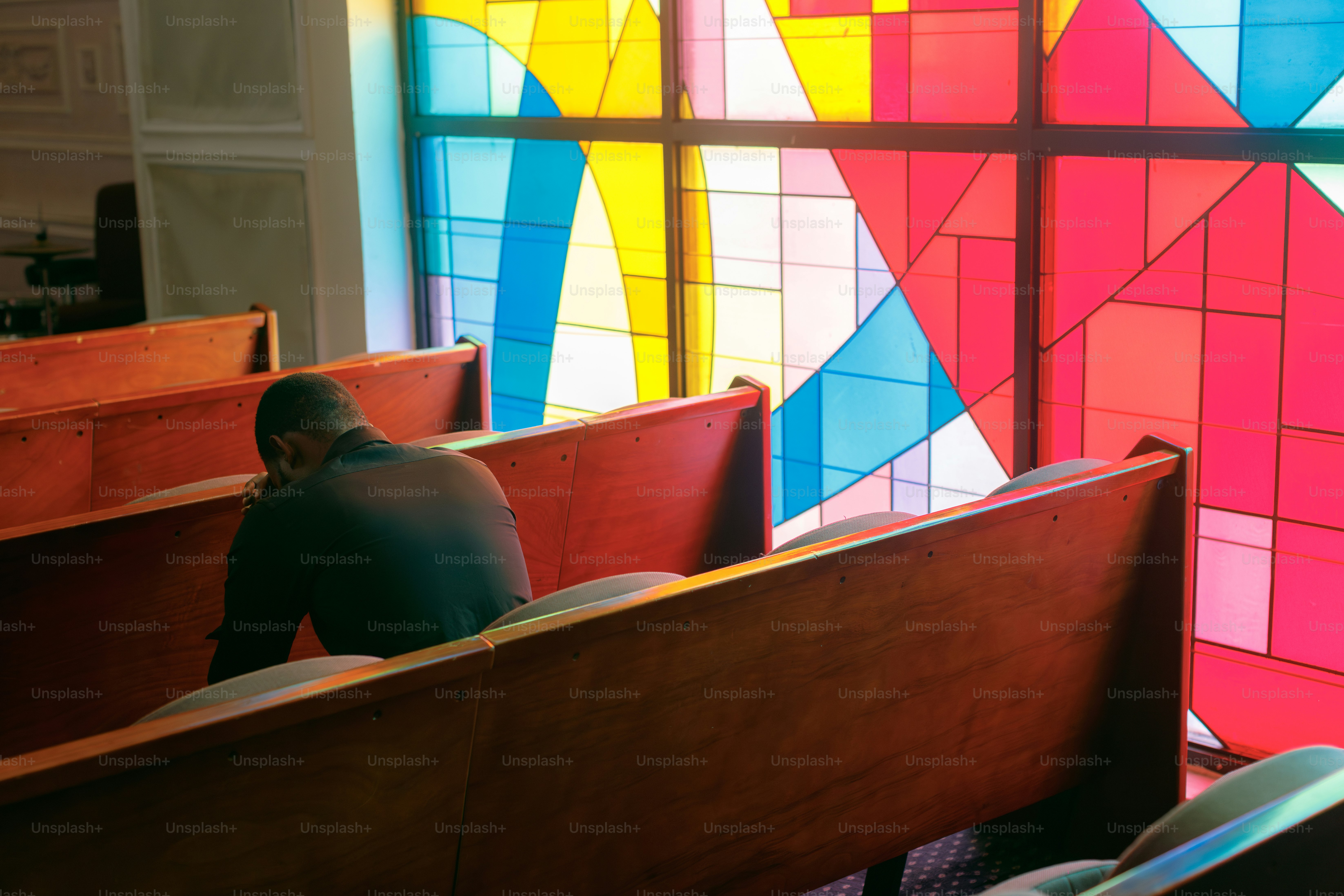 ステンドグラスの窓のそばで教会のベンチに座る男性