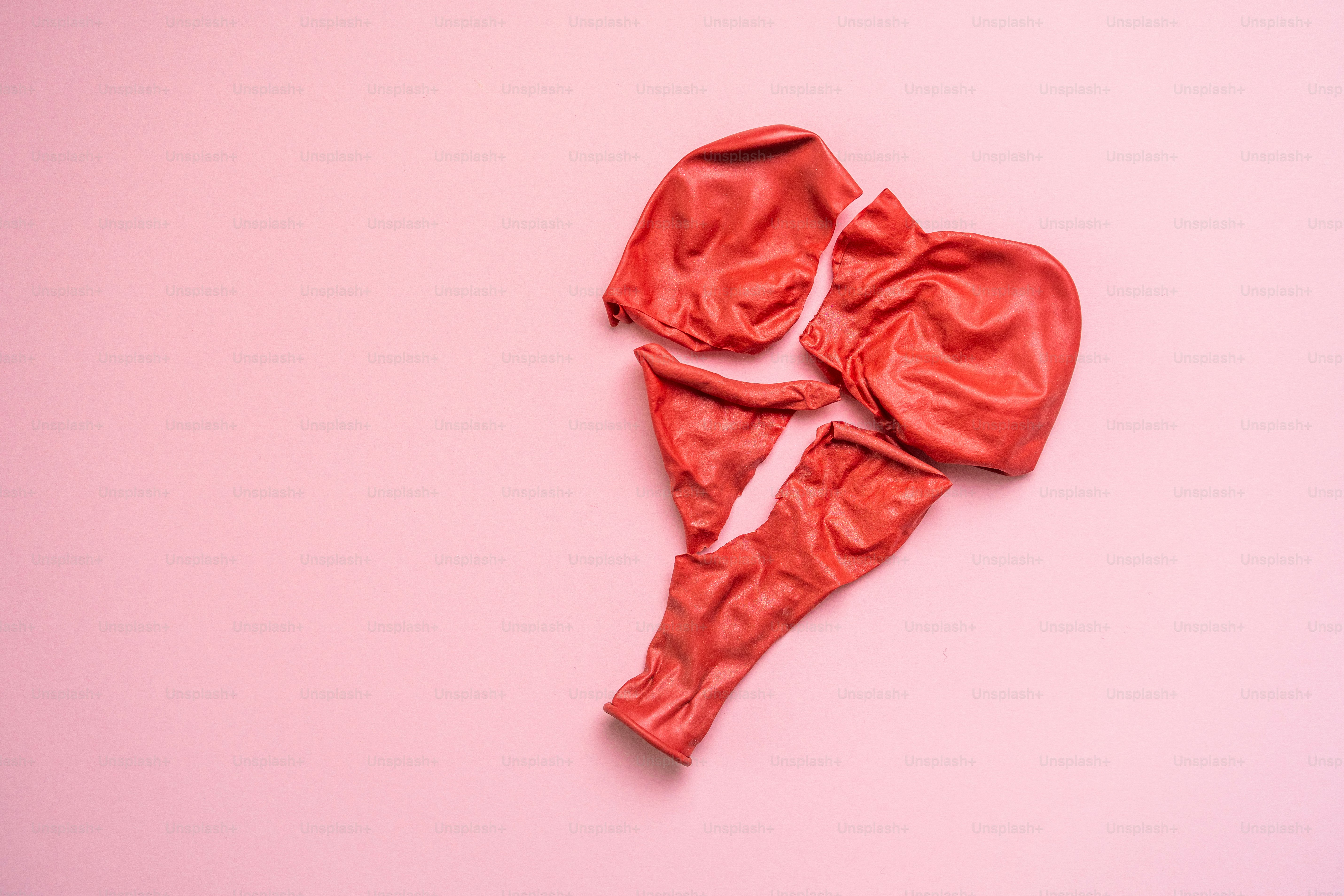 A deflated and broken red balloon on a pink background