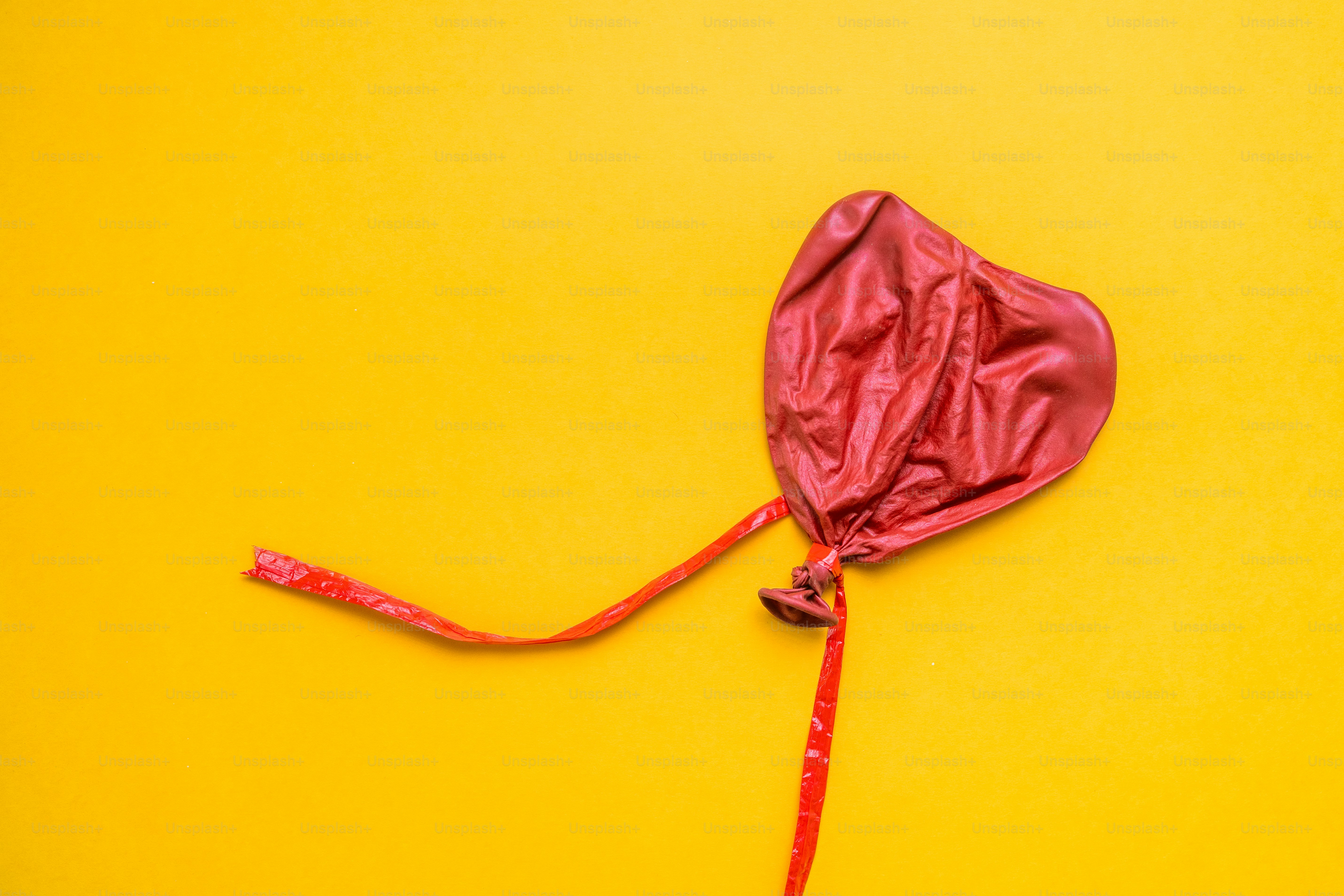 A deflated red heart-shaped balloon on a yellow background