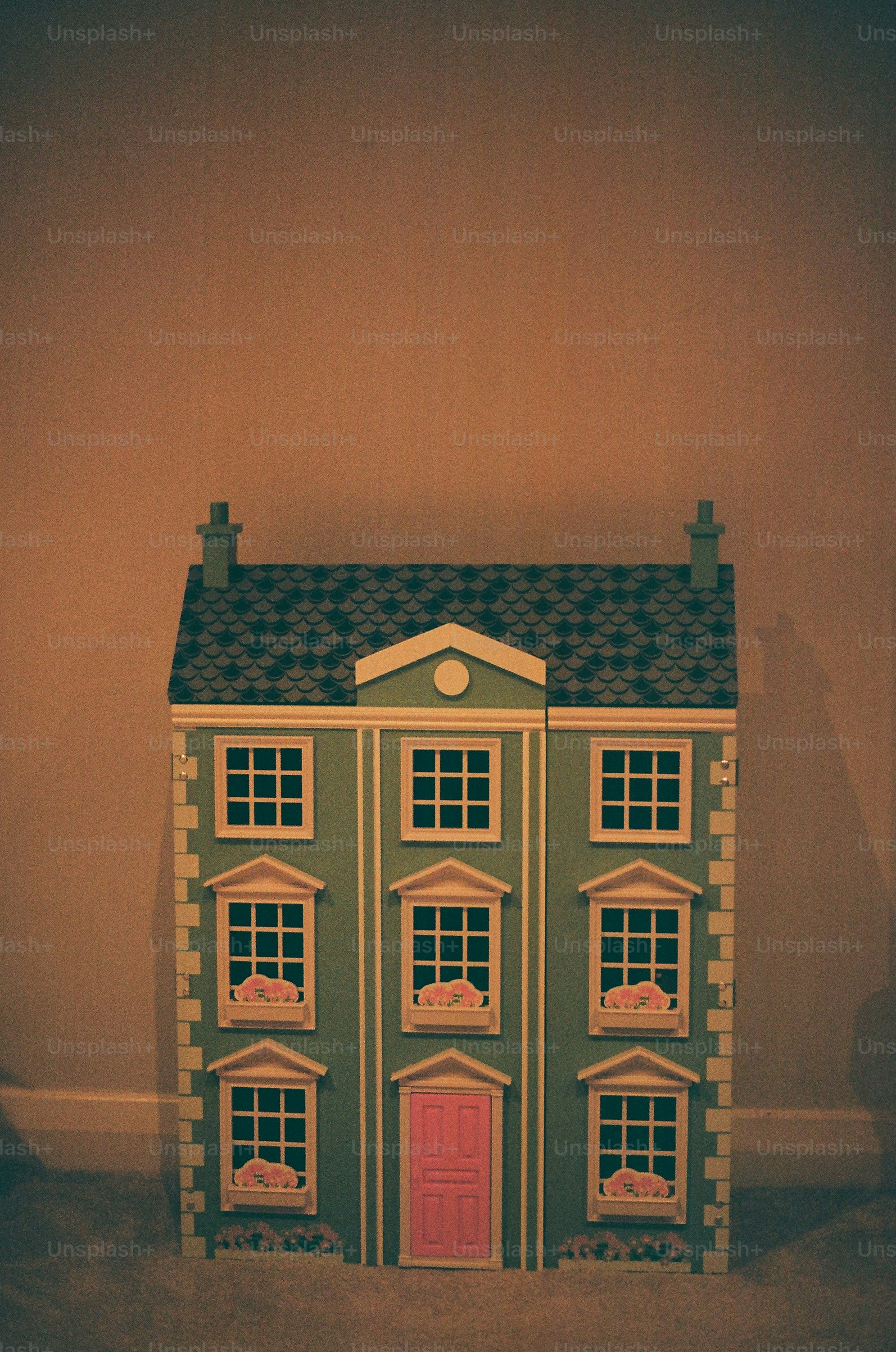 A dollhouse with a pink door and white windows