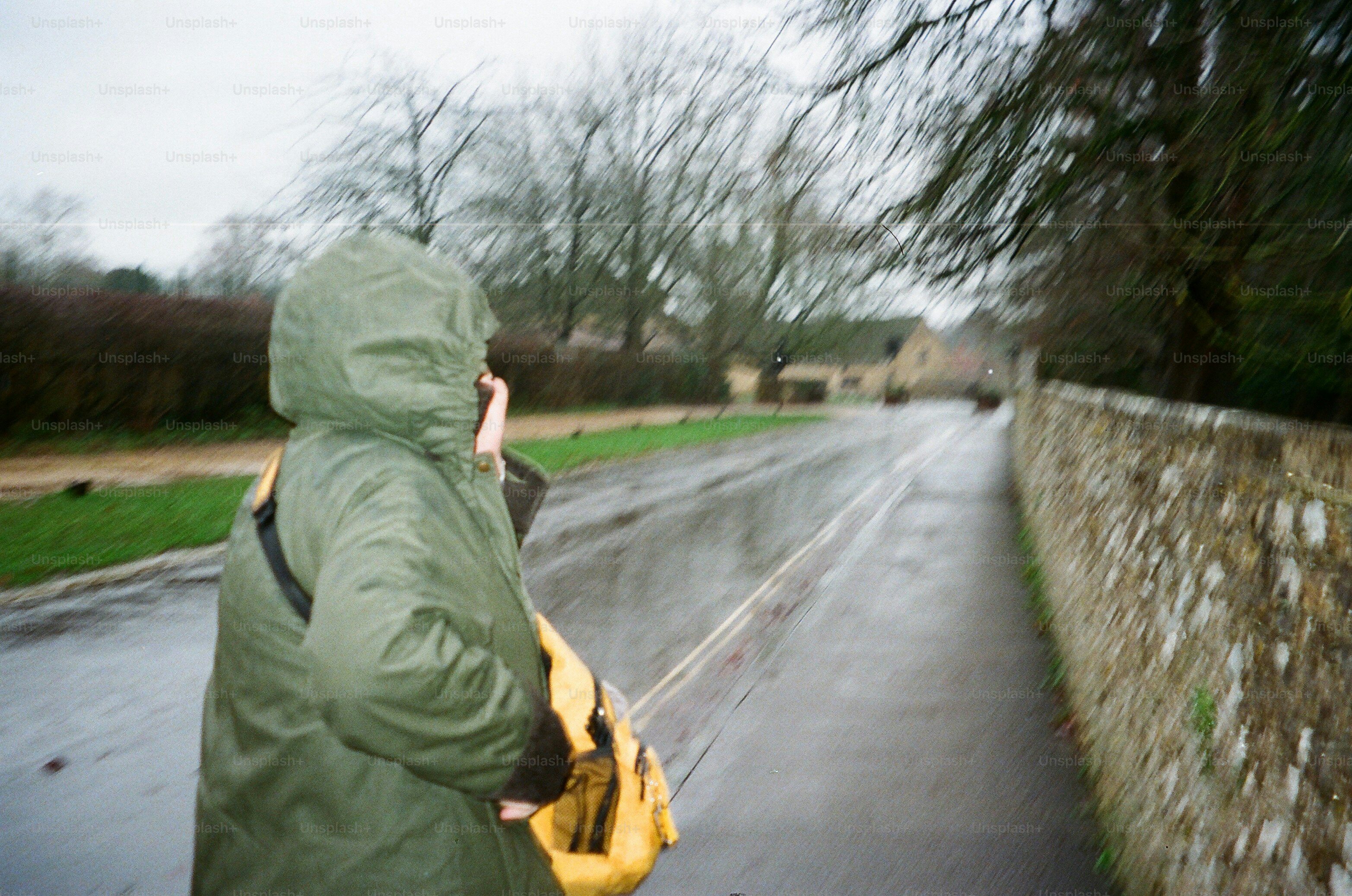 Person in raincoat walks on wet road in village.