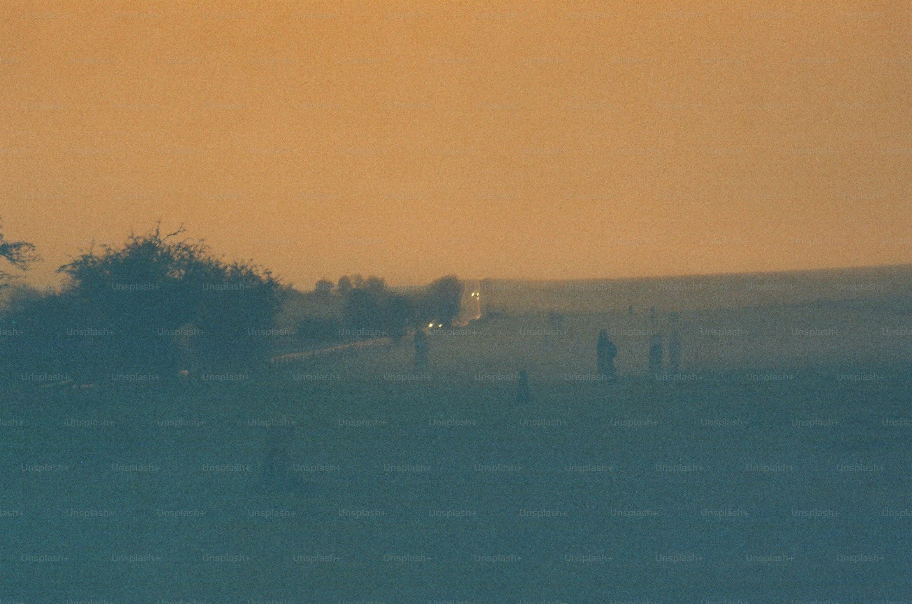 Distant figures walk along a road at dusk.