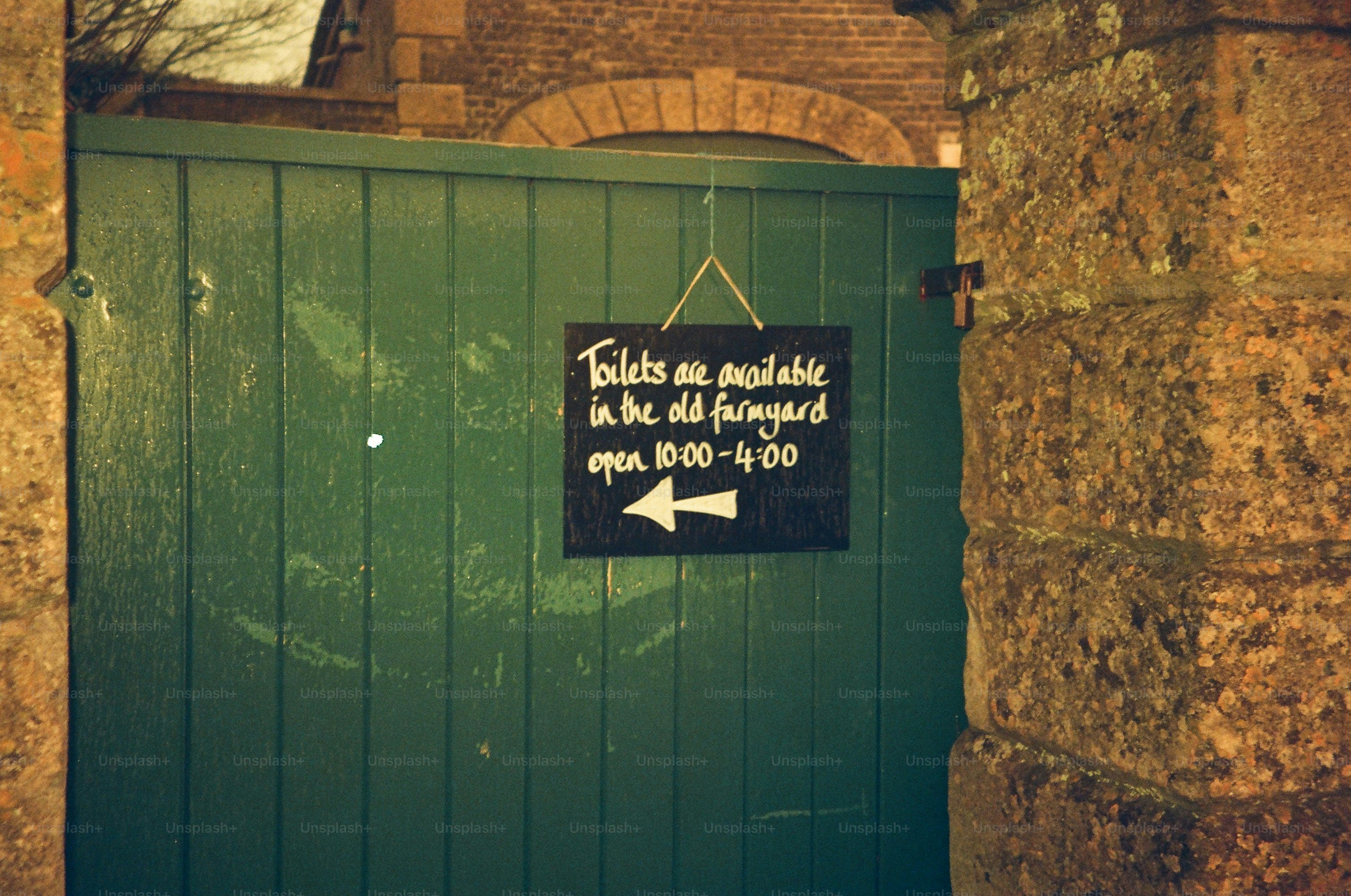 Green wooden gate with a sign pointing left.