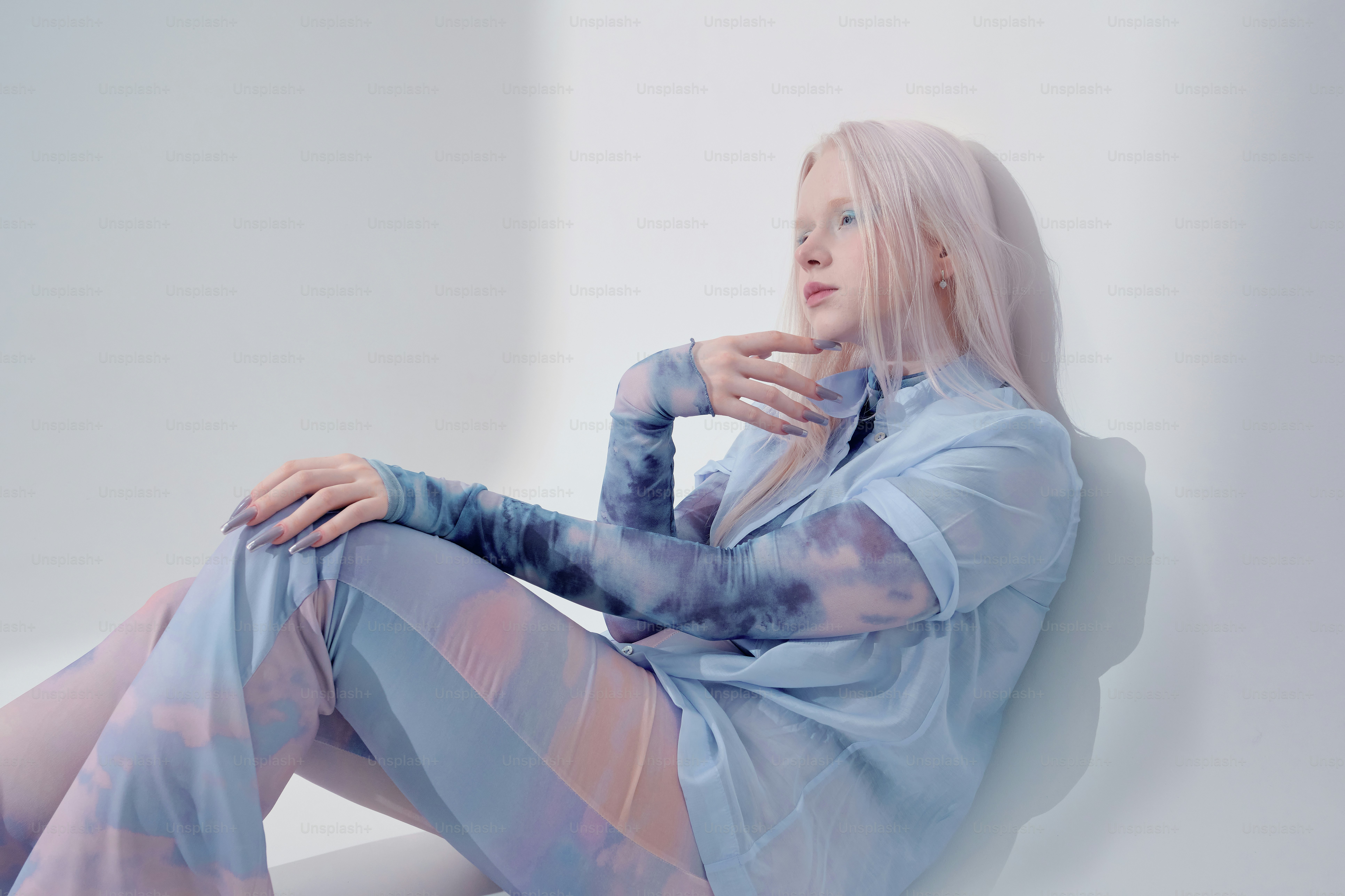 A woman with pink hair sits against a white wall. photo – Blue Image on ...