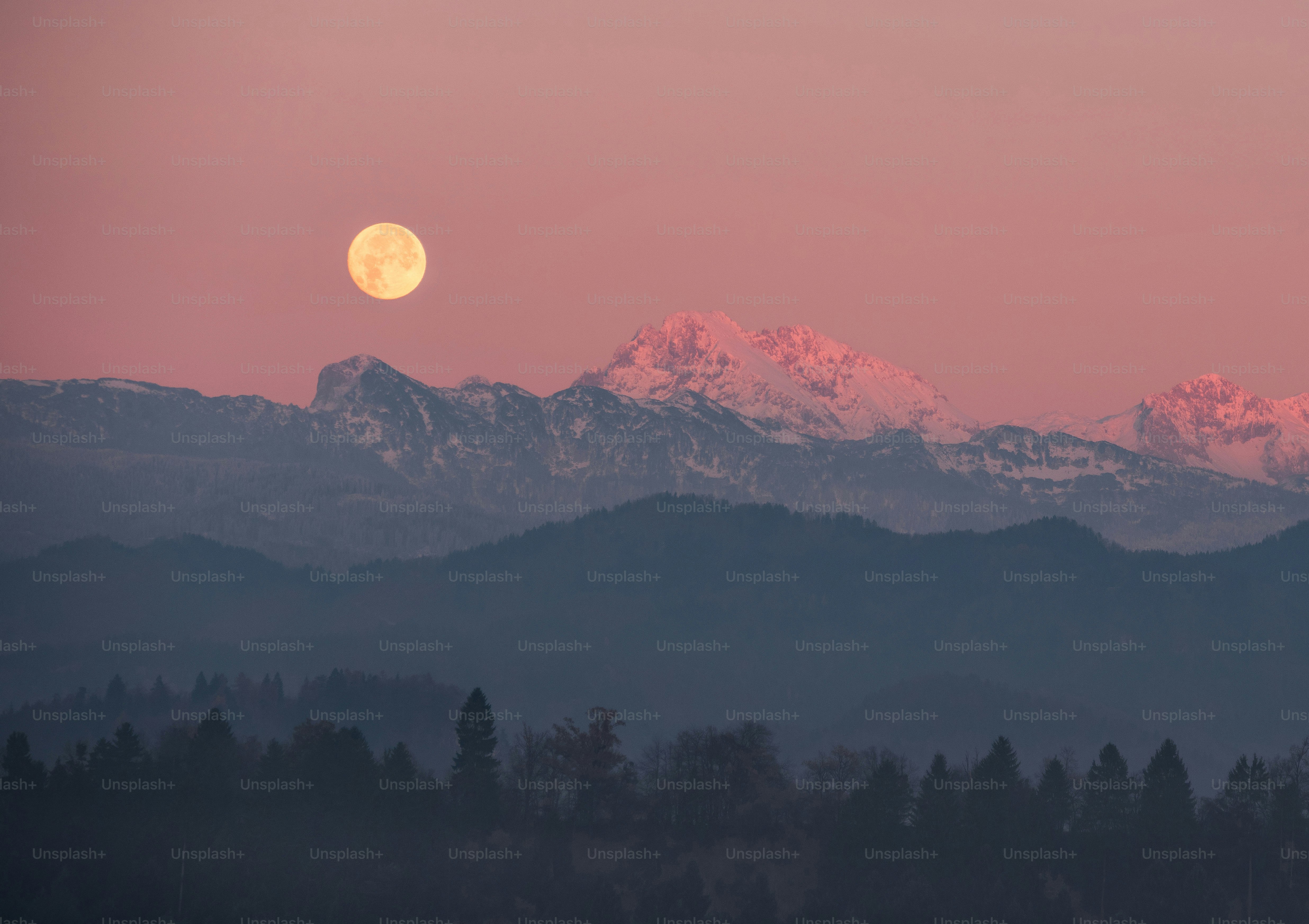 La pleine lune se lève au-dessus des montagnes enneigées au crépuscule.