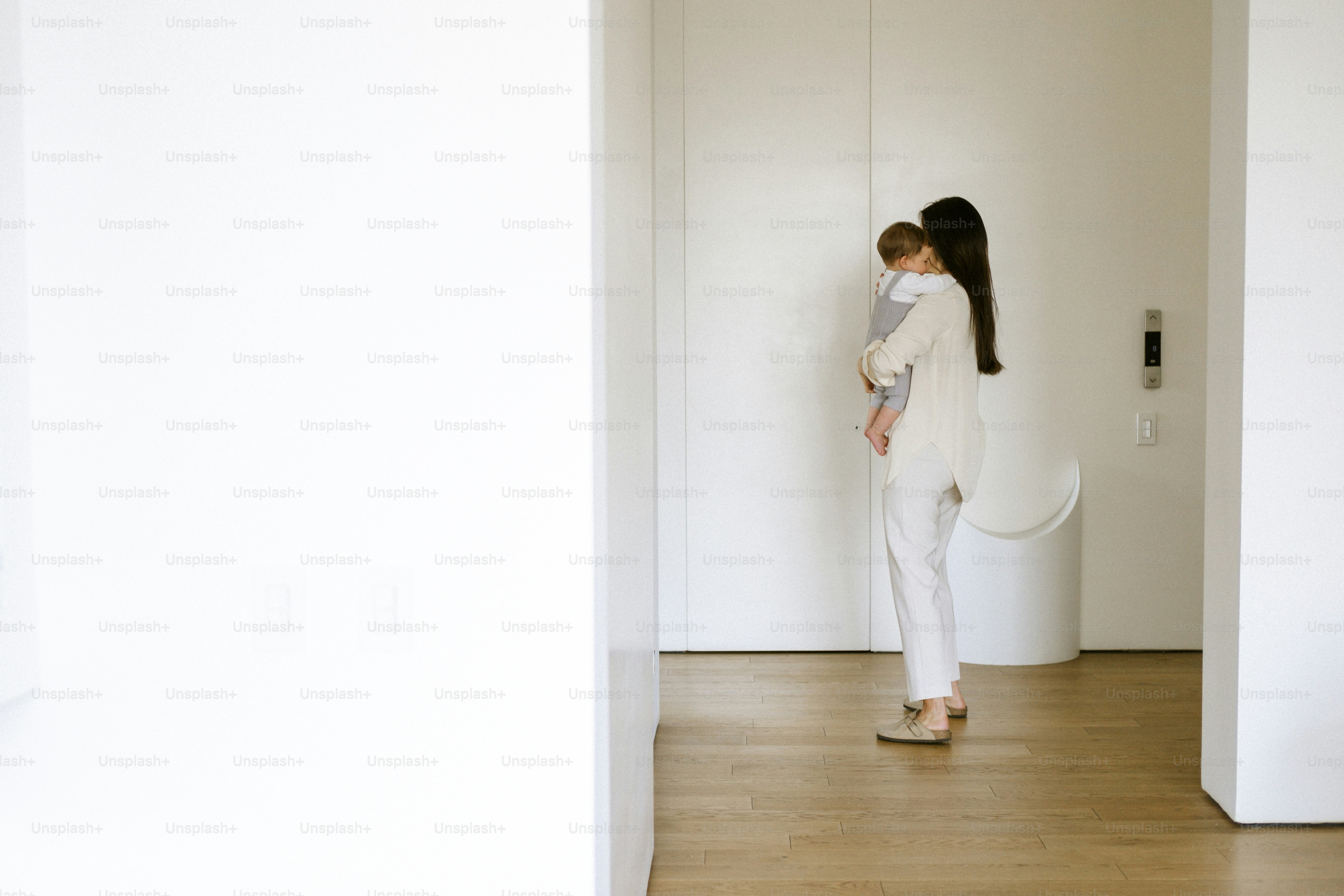 Woman holding baby in a modern, minimalist hallway.