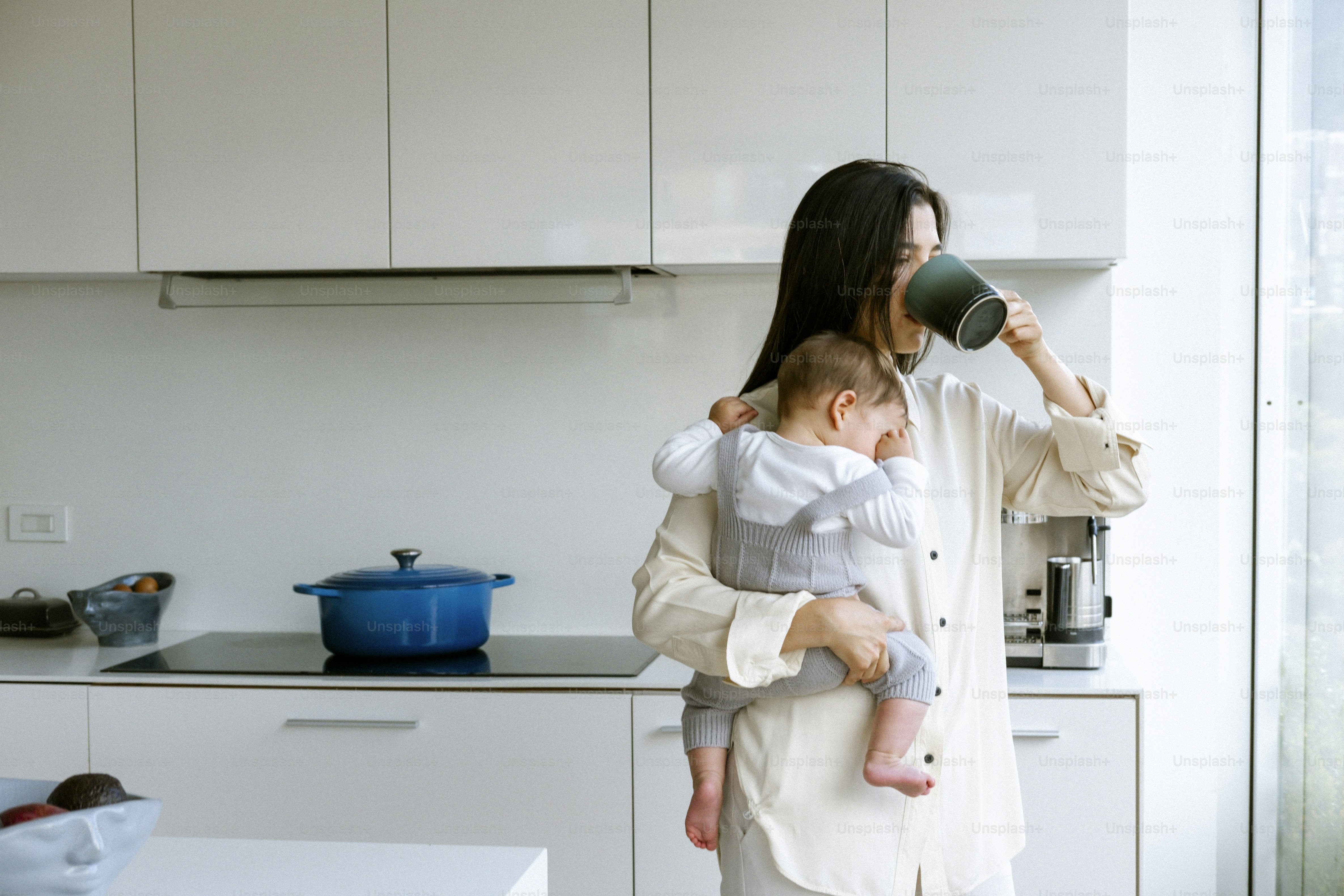 Woman drinking coffee while holding a baby.