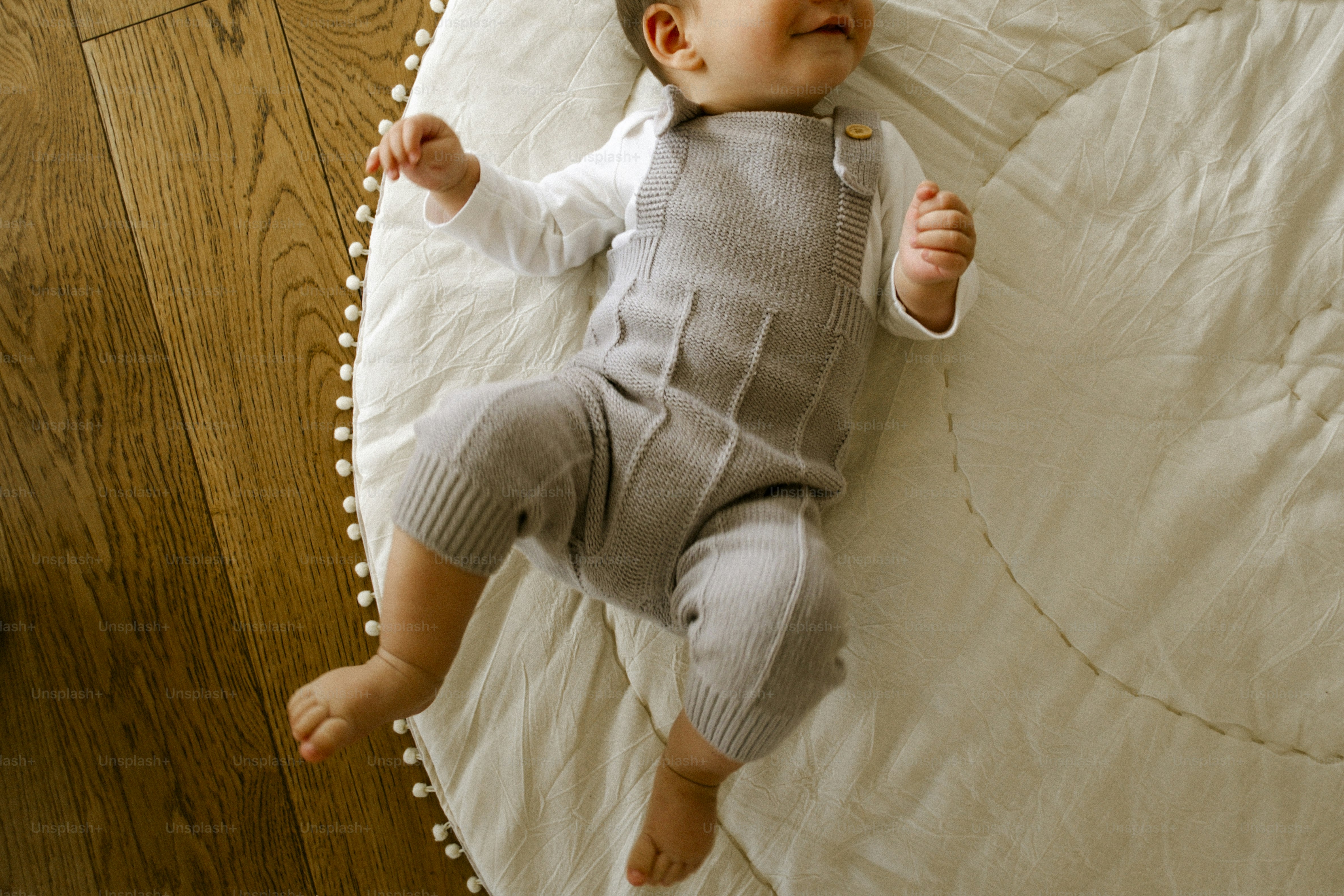 A baby in a grey romper lies on a mat.