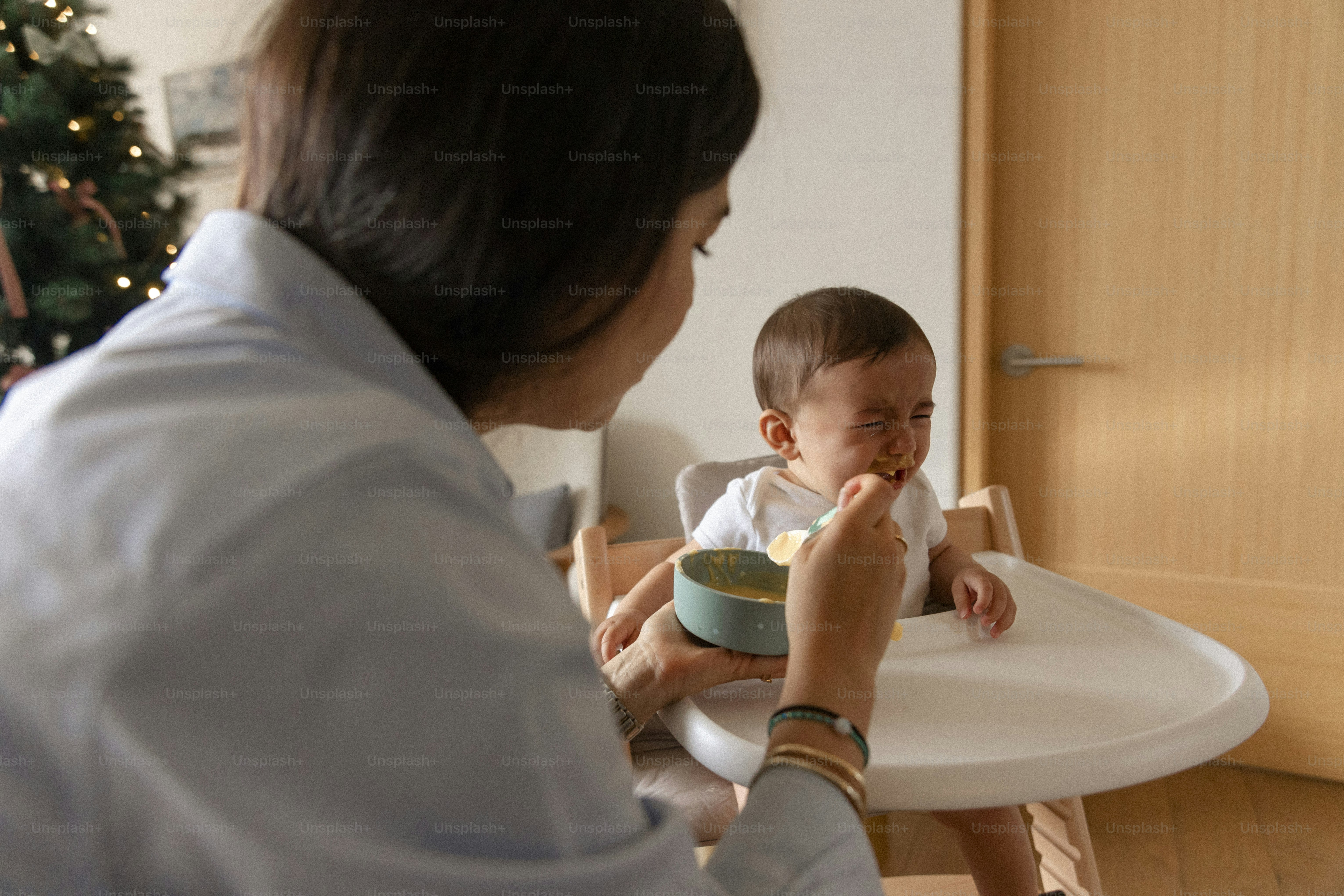Mother feeding baby in high chair with spoon