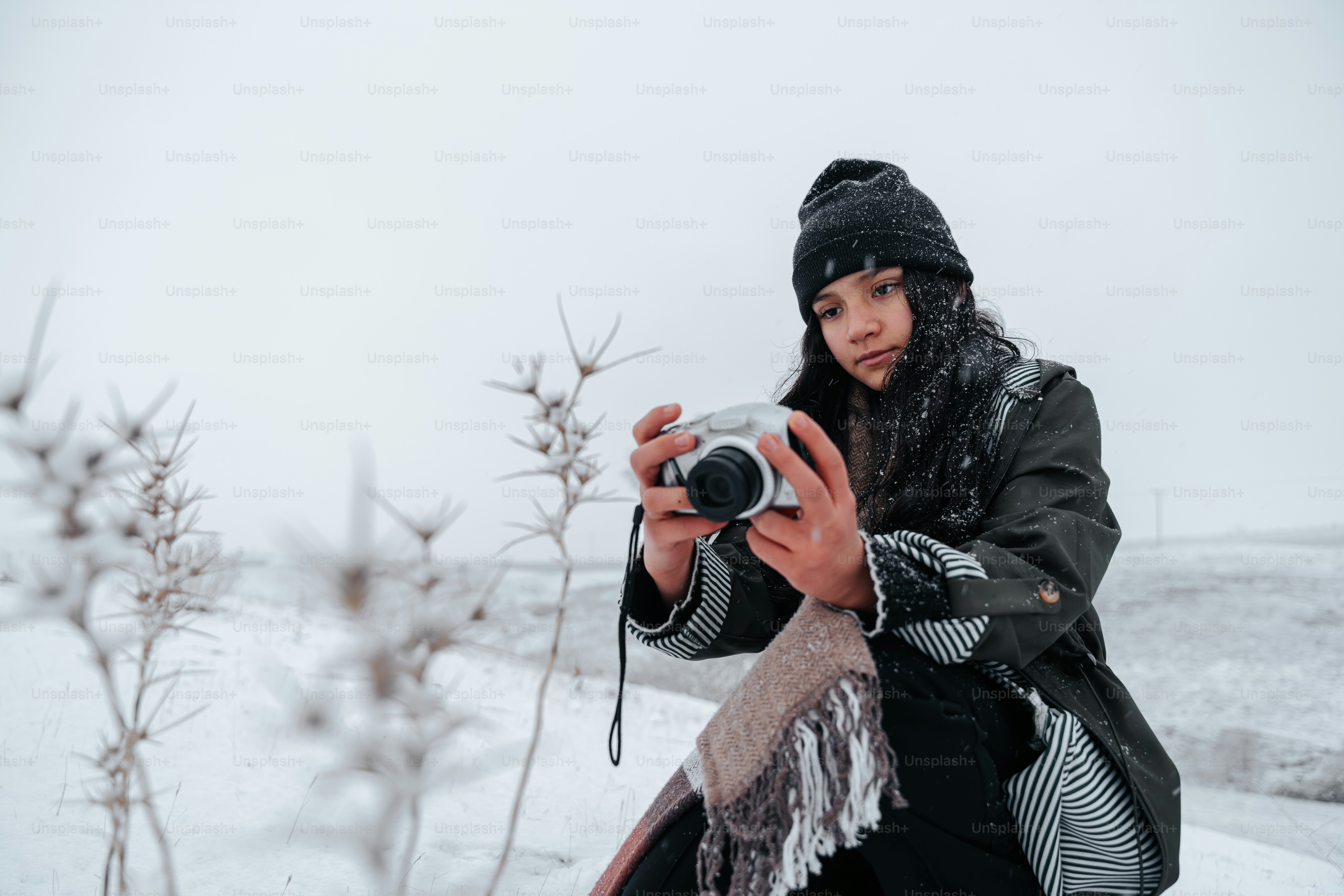 A young woman holds a camera in a snowy landscape.