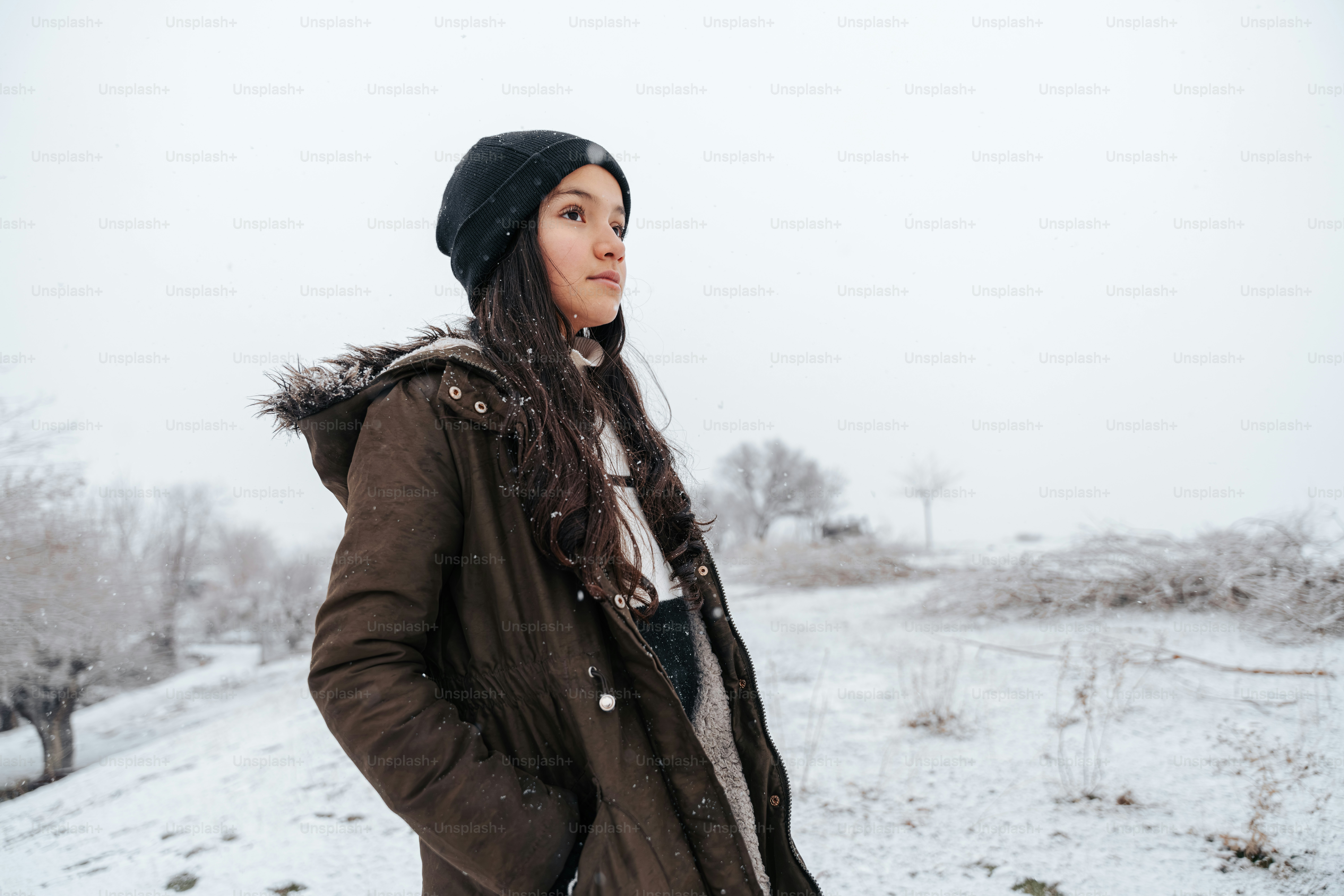 Young woman in winter coat looking out over snowy landscape