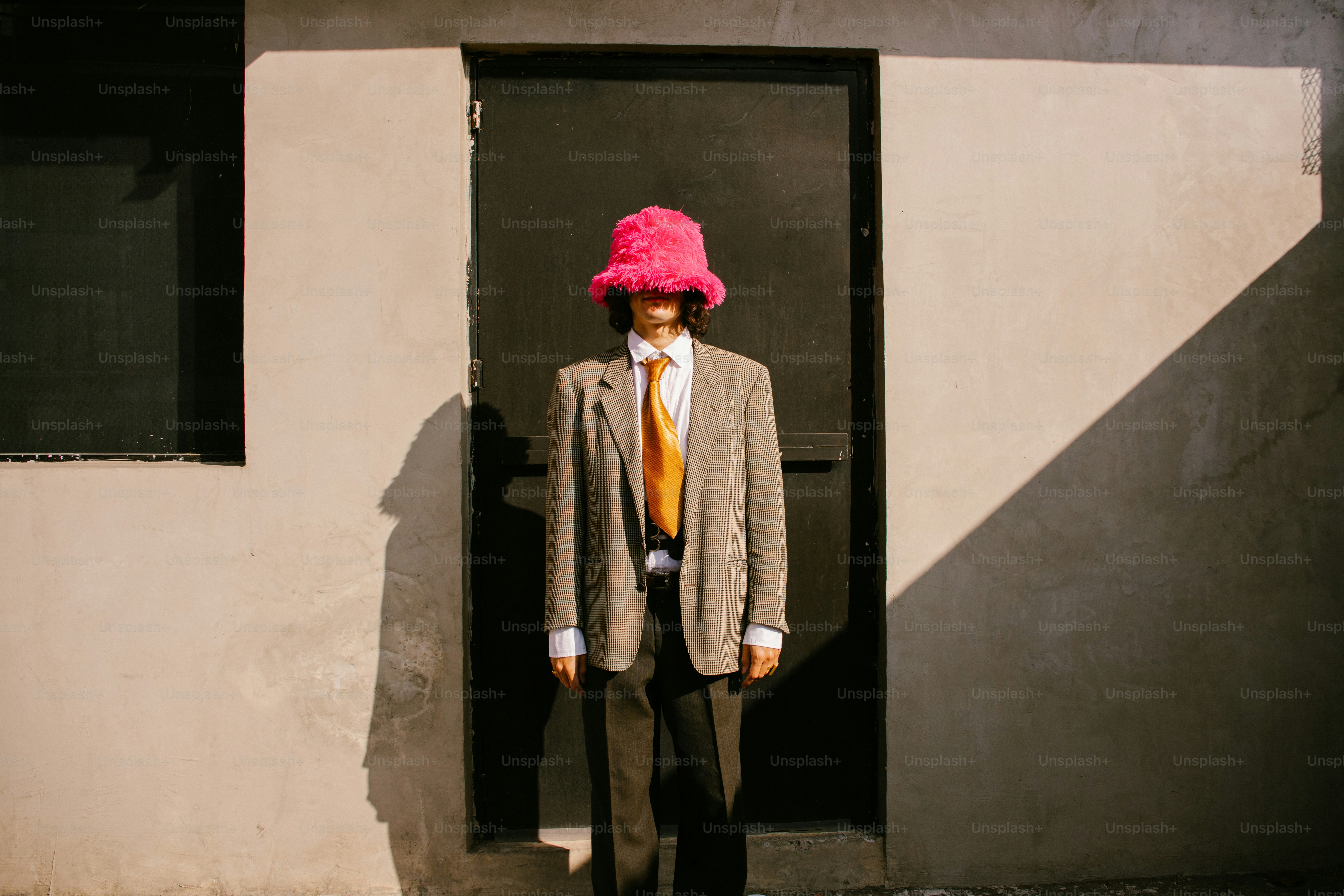 Una persona in abito e cappello rosa a secchiello sta vicino alla porta.