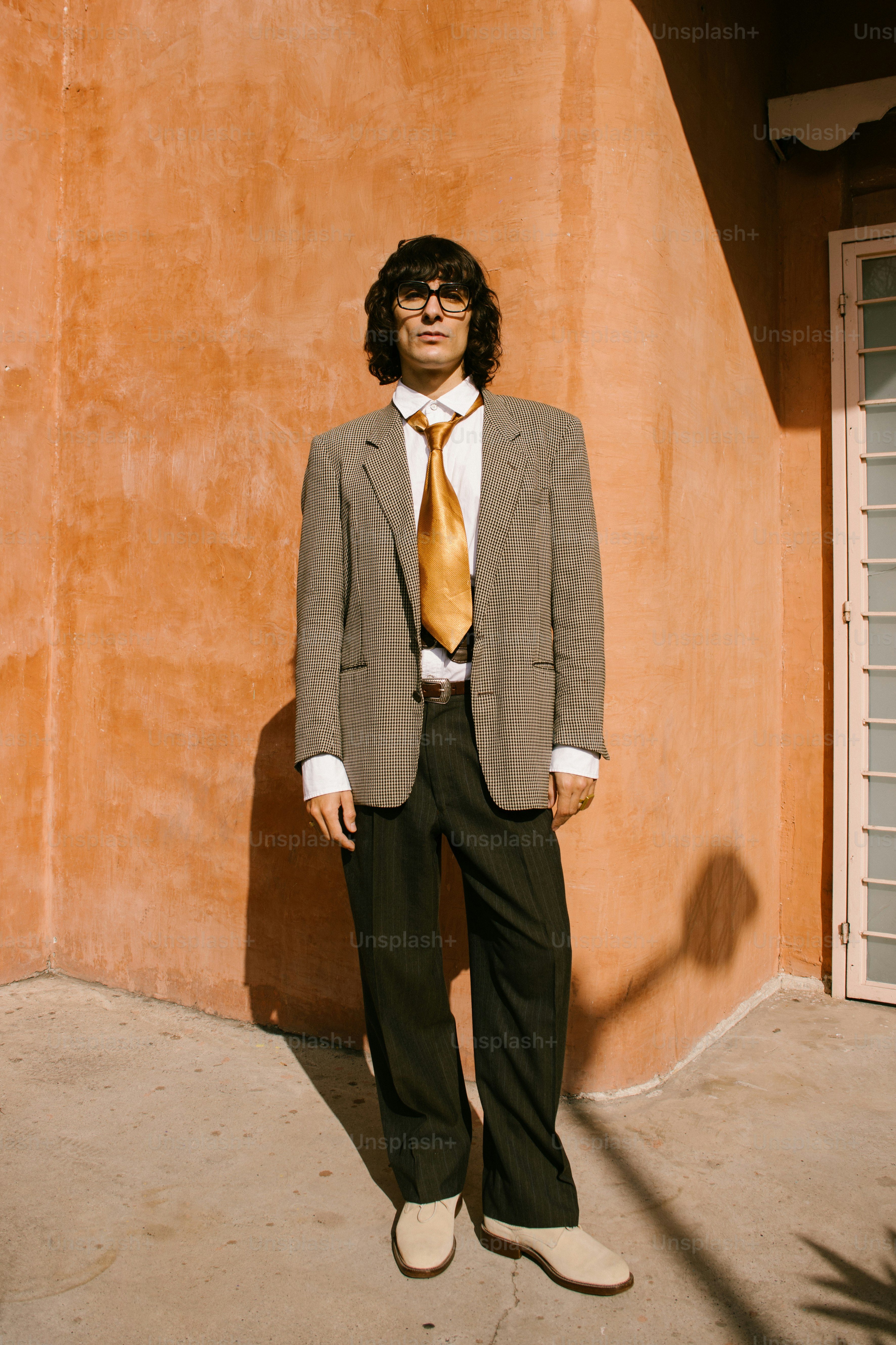 Man in suit and tie stands against orange wall.