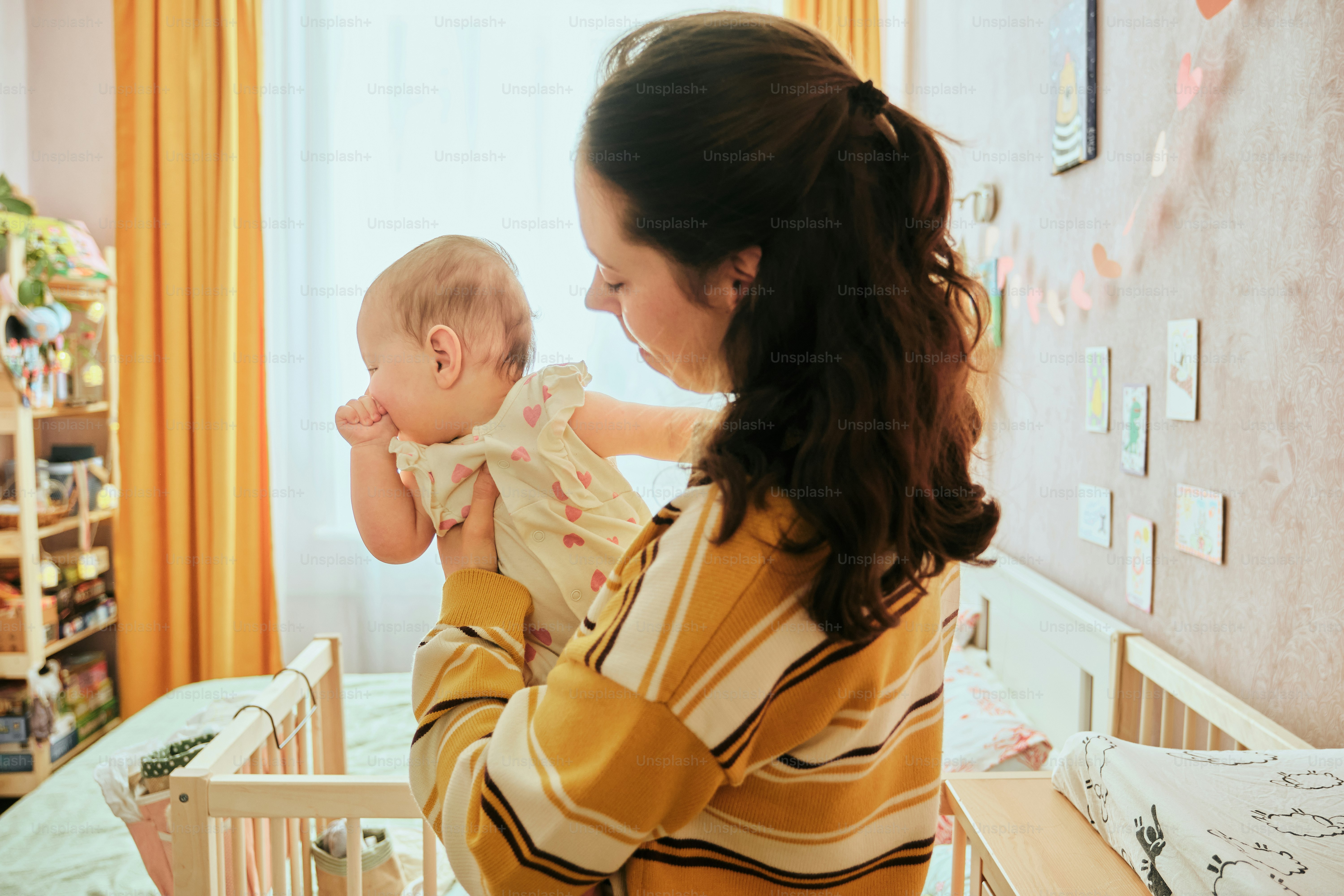Mother holding her baby near a crib