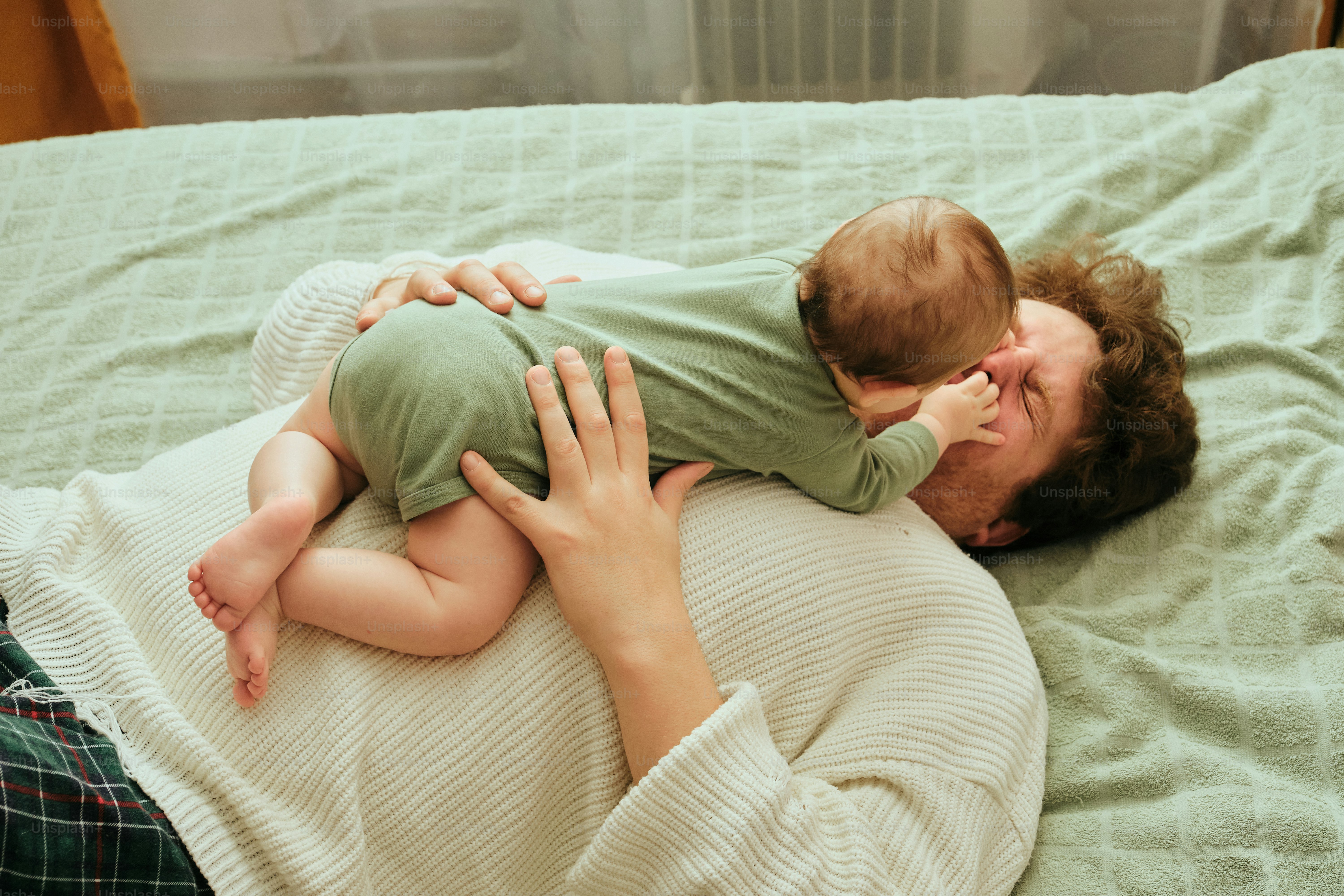 Baby lying on parent's chest, embracing face down on bed.