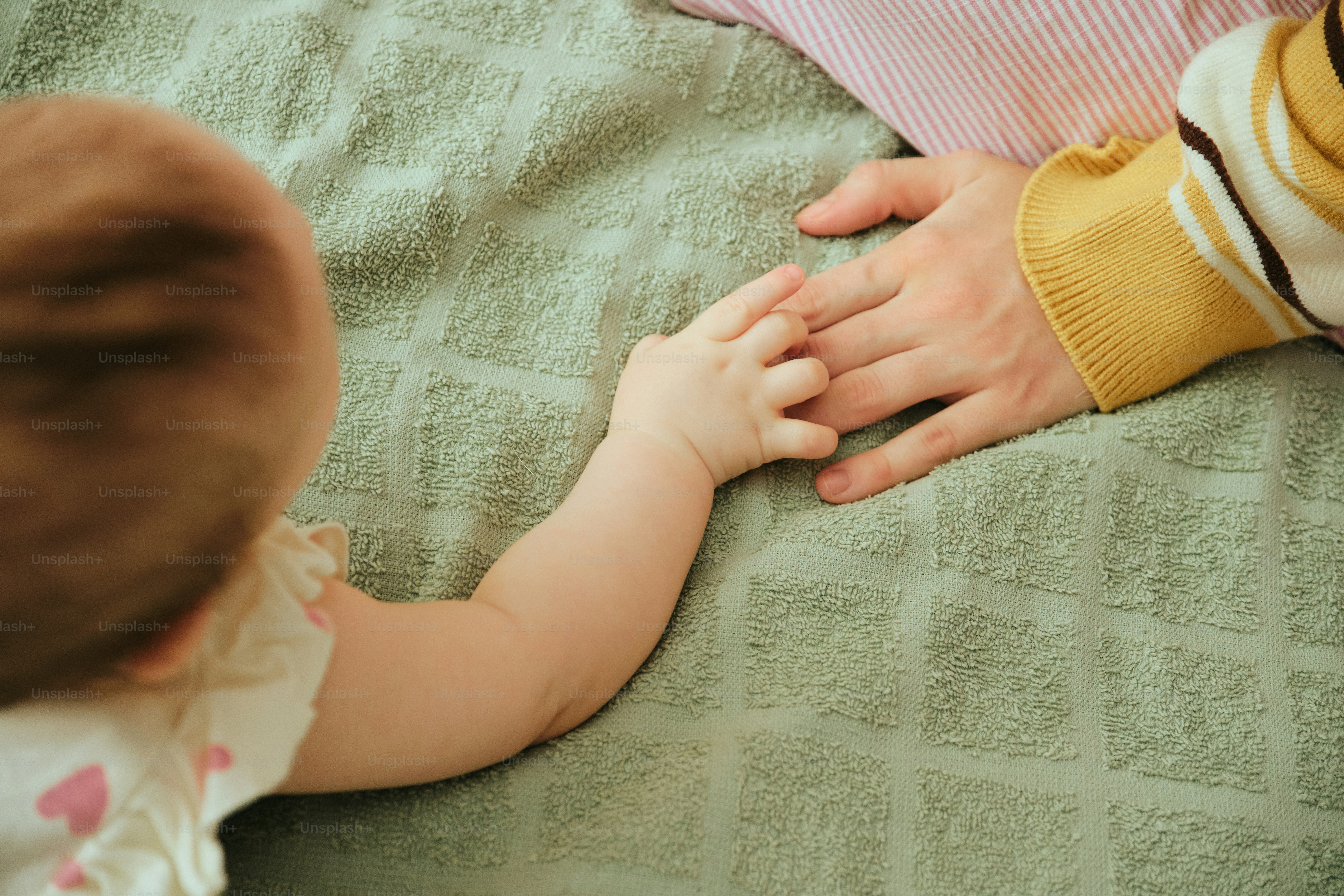 Baby holding an adult's finger on a green blanket