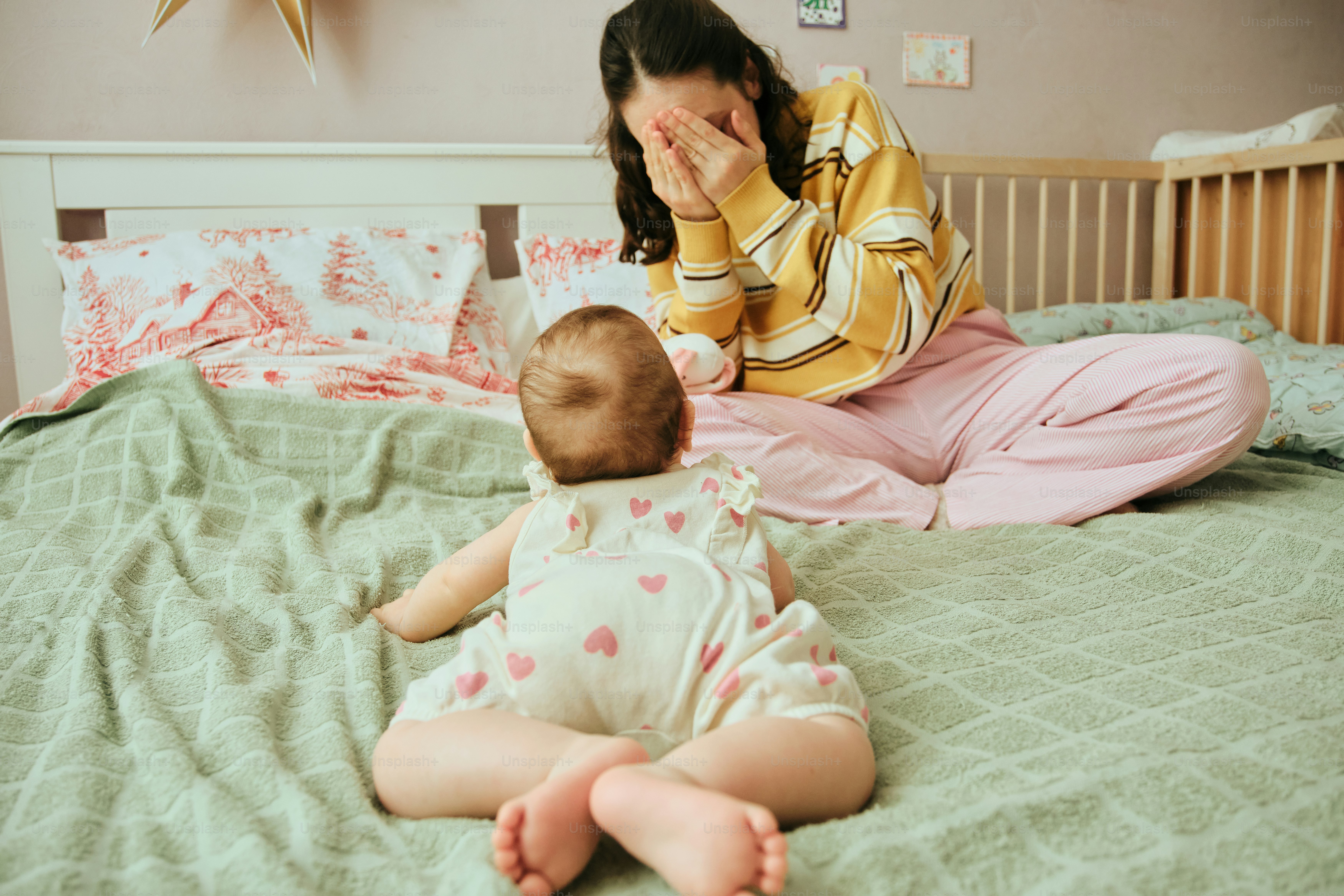 Mother covering face while baby lies on bed