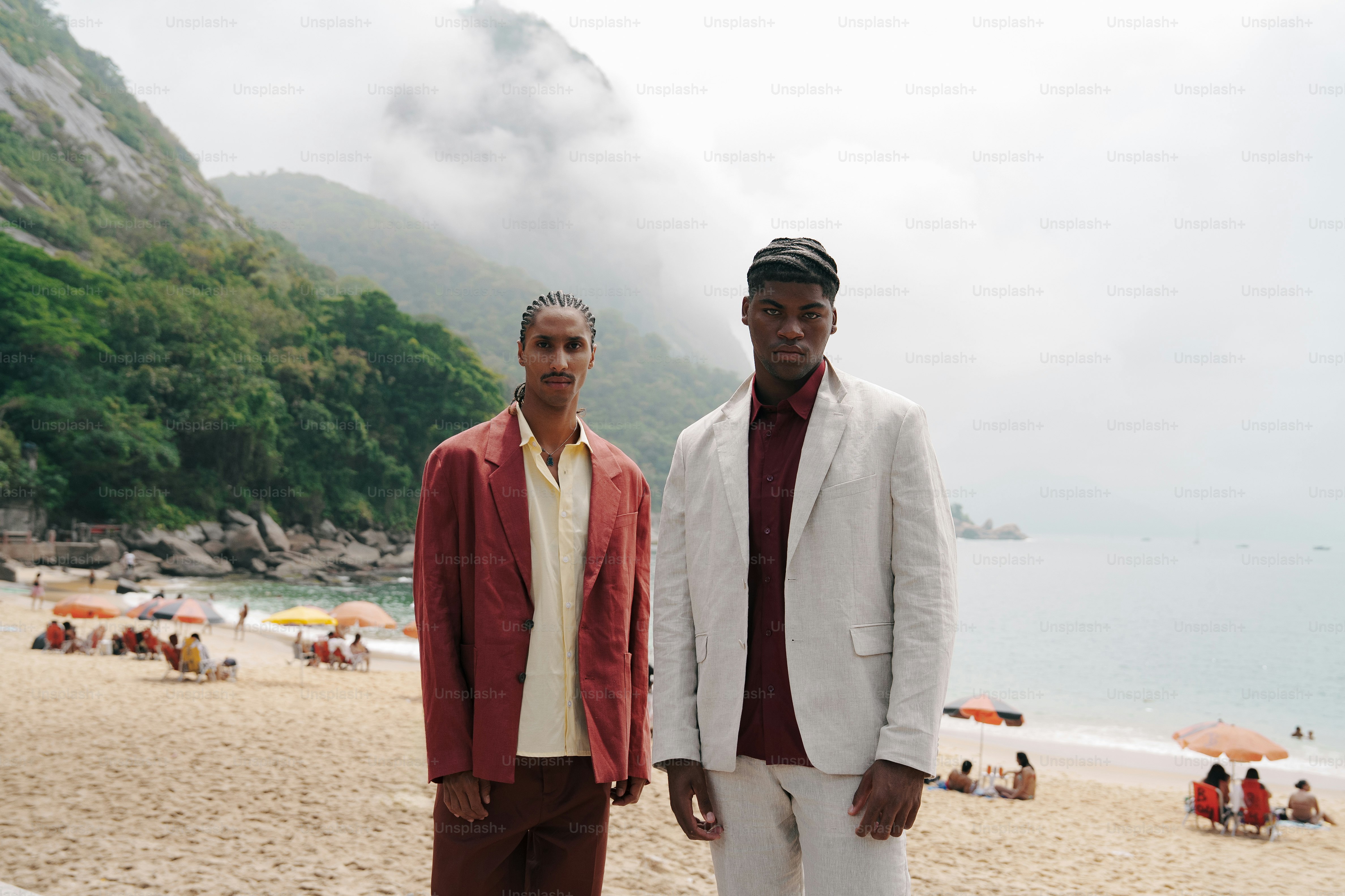 二人の男が海と山々のある浜辺に立っている。