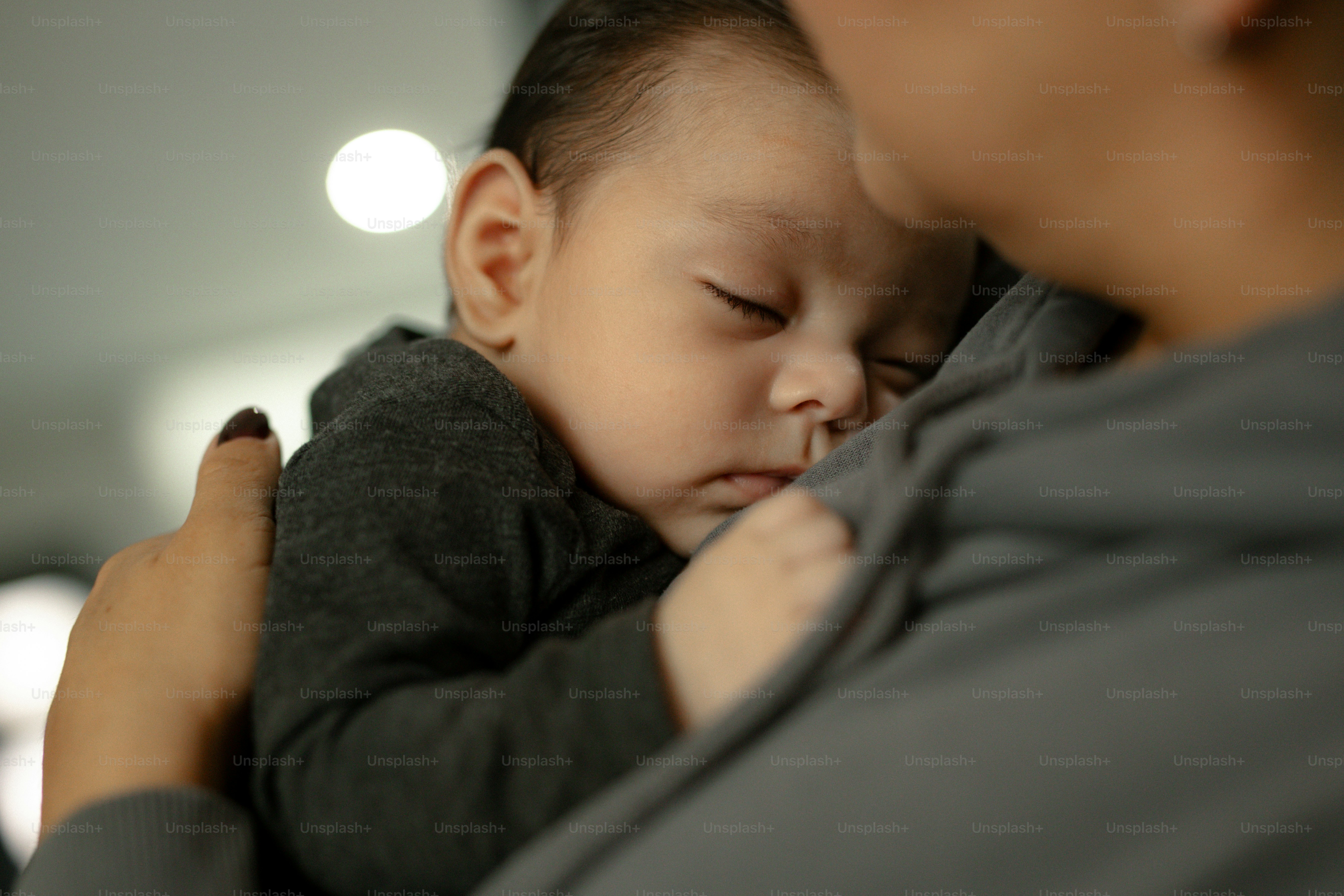 Um bebê dormindo descansa nos braços de um dos pais.