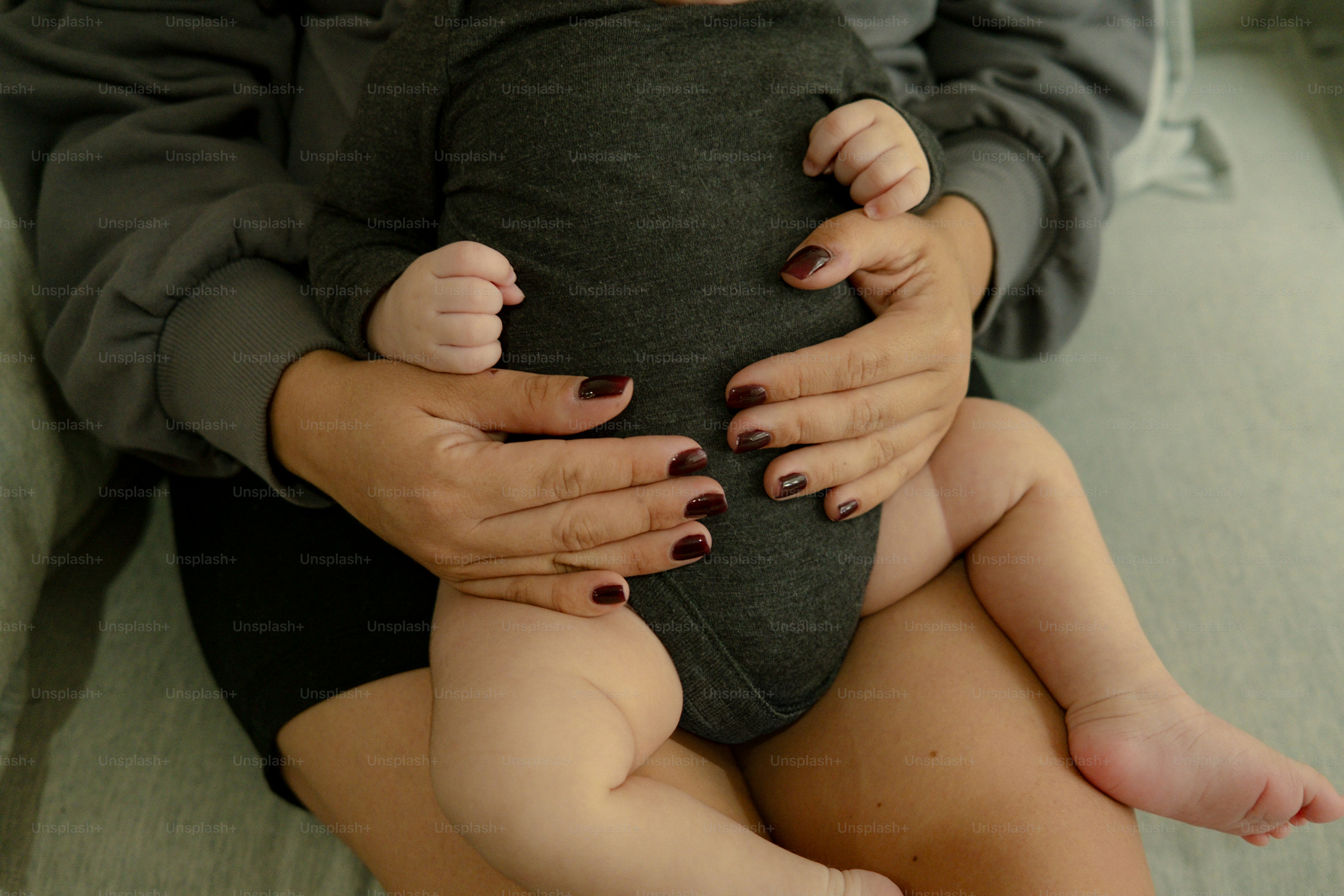 Uma pessoa segura um bebê usando um macacão cinza escuro.